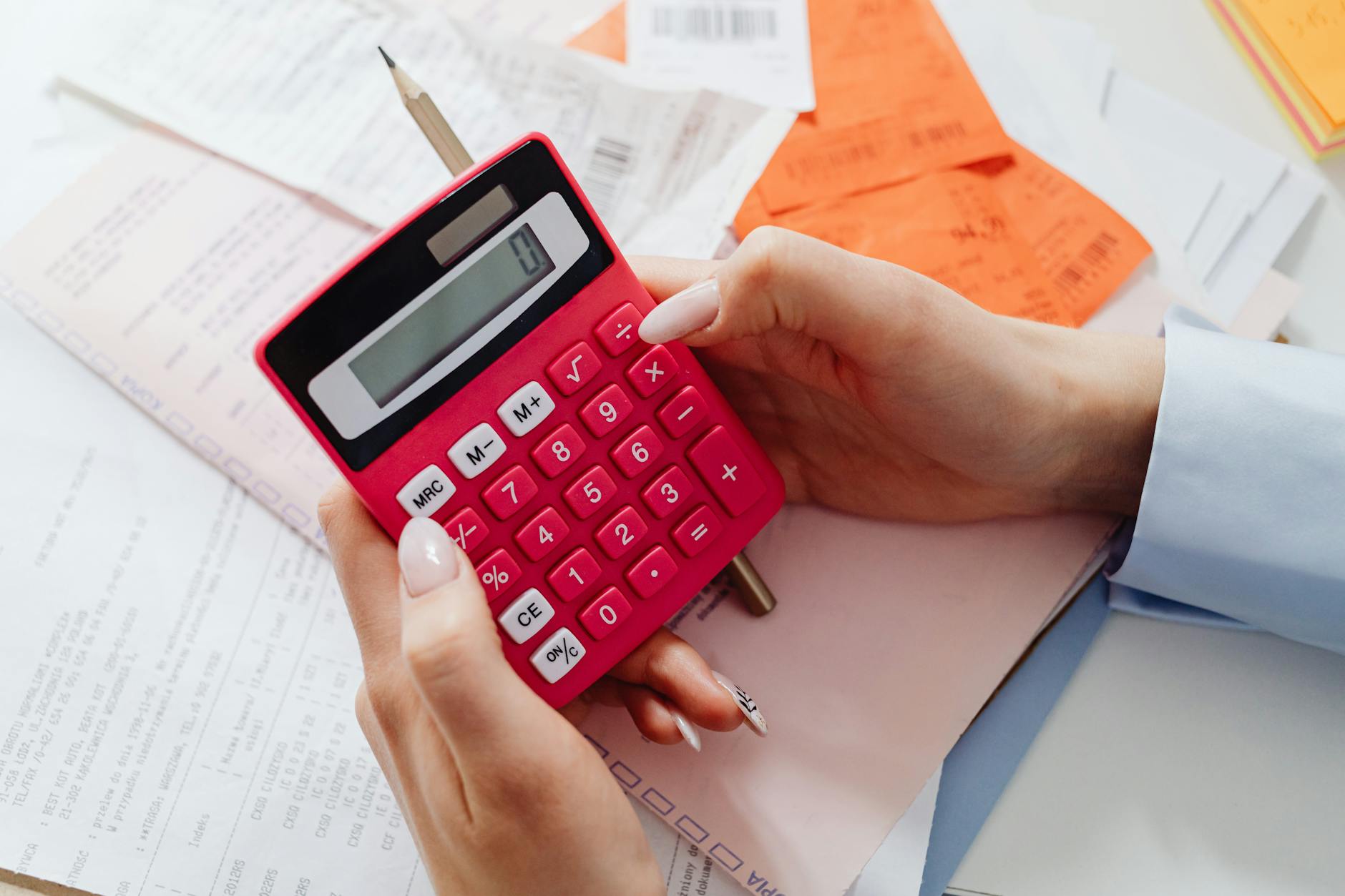 Close-up of hands holding a red calculator, managing finances with documents and receipts. - calorie deficit calculator