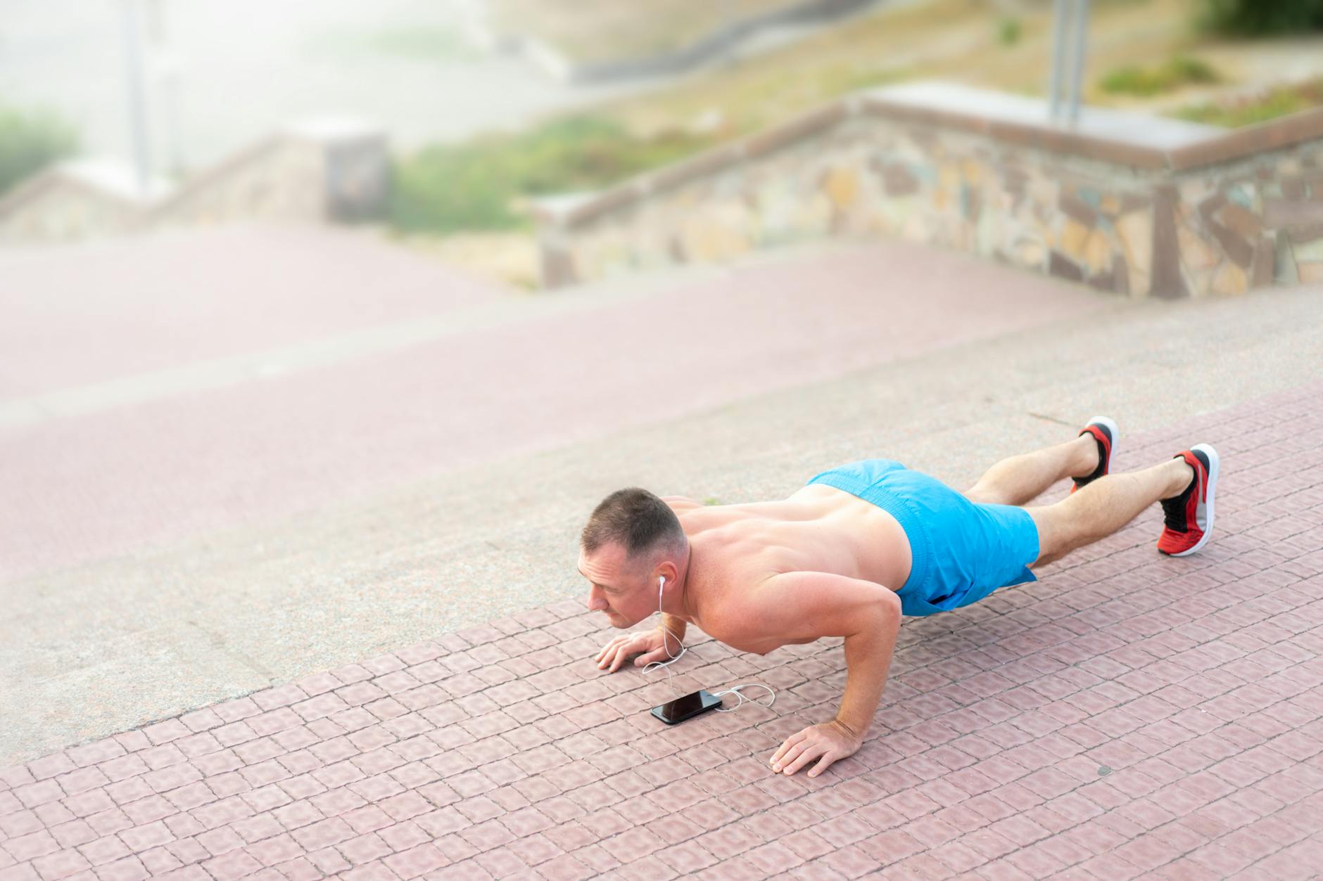 A fit man listening to music and doing push-ups outside on stairs. - cardio workouts for men