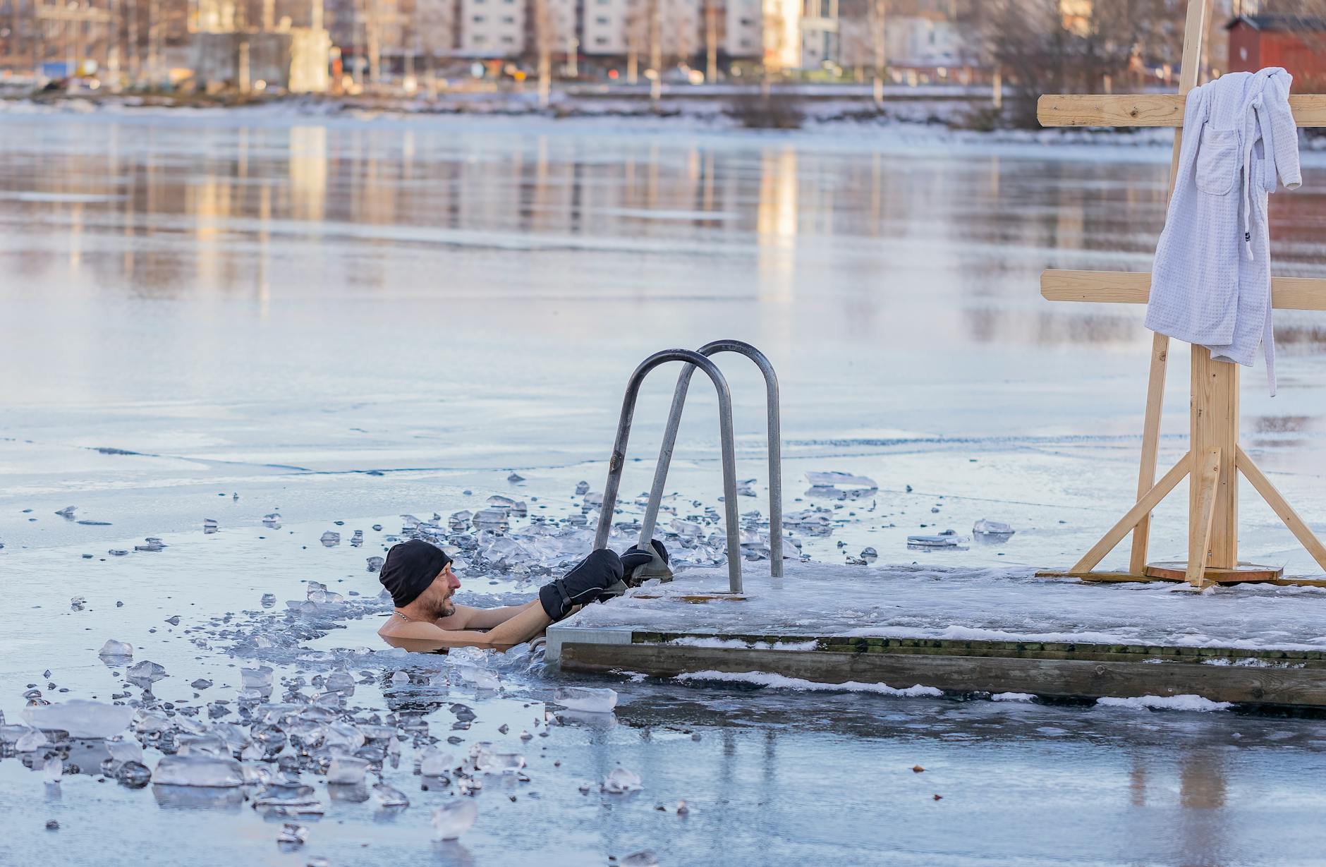 Man in icy water near a wooden dock with towel in the winter landscape. - cold water swimming benefits