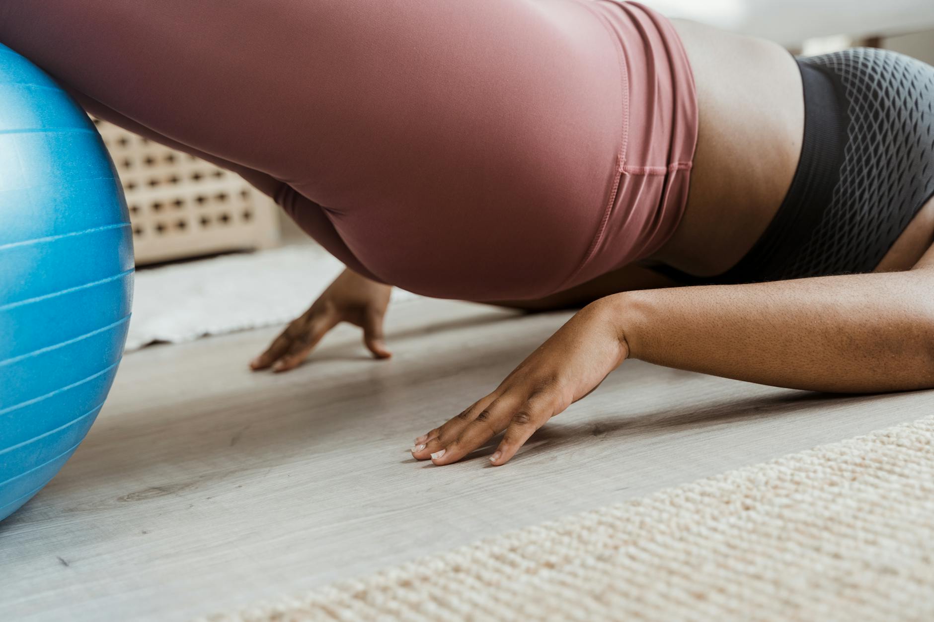 Close-up of a woman working out indoors using a fitness ball. Focus on balance and core strength. - core workout at home