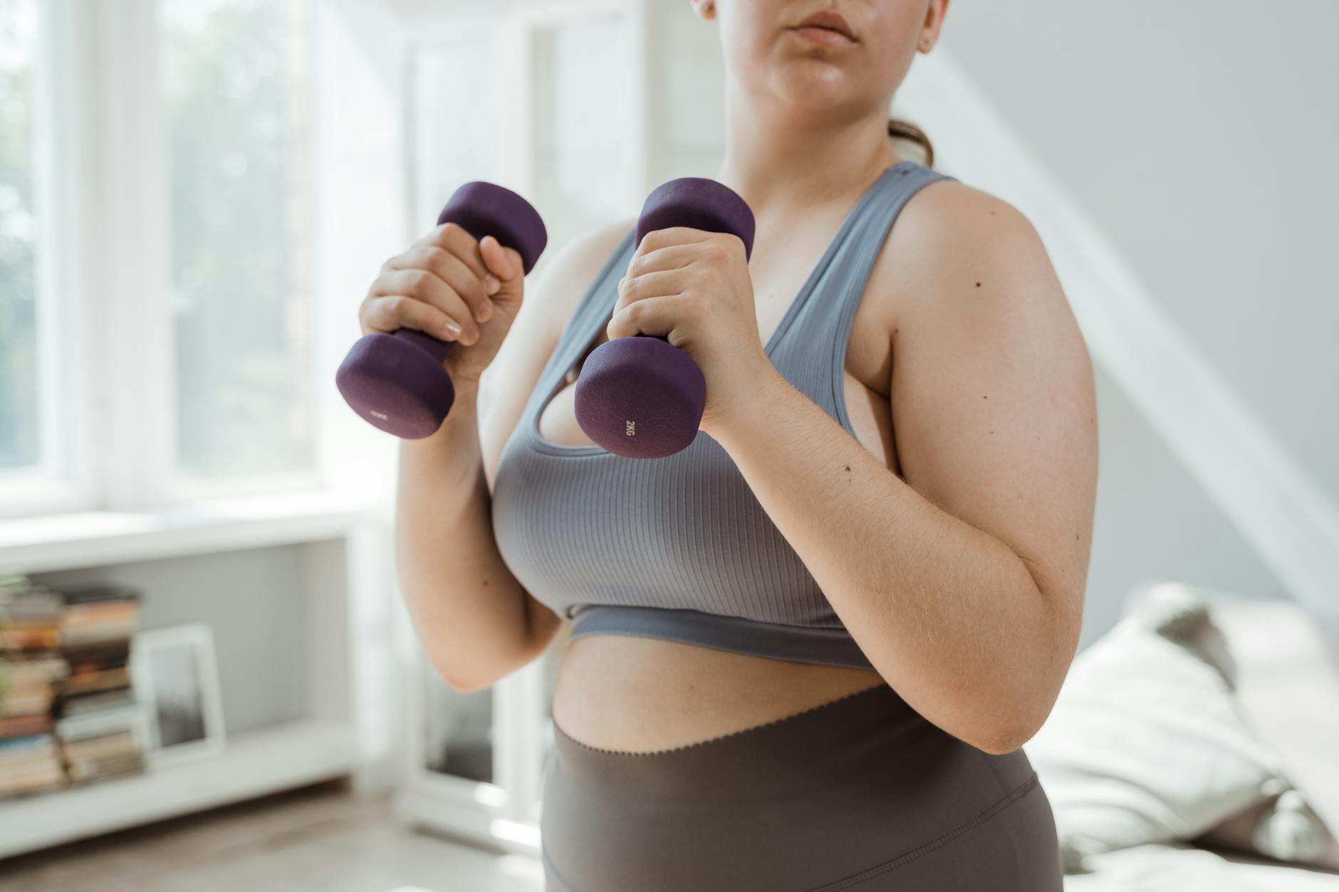 Plus size woman in activewear working out with dumbbells indoors, promoting body positivity. - dumbbell good morning