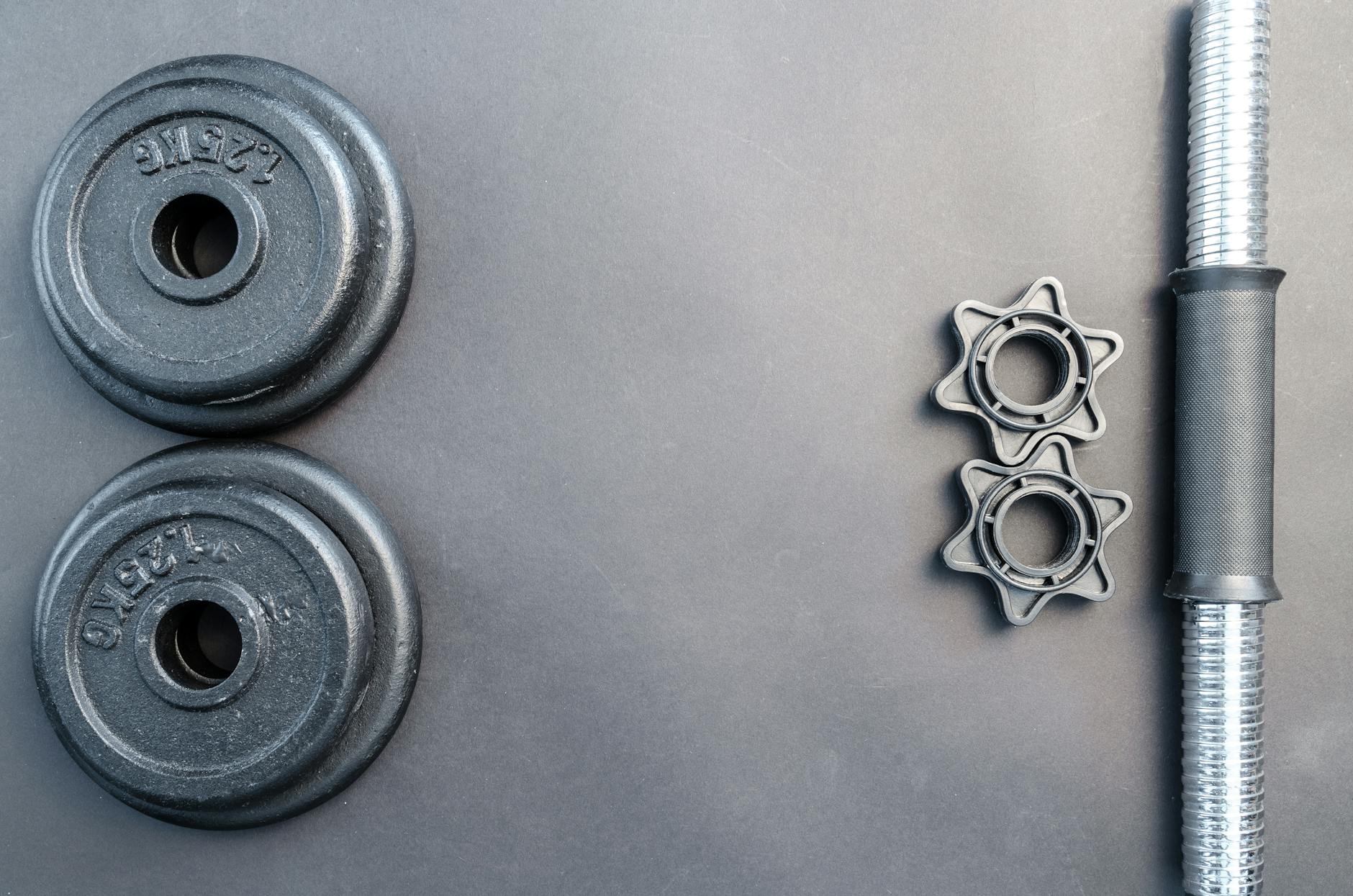 Barbell and two dumbbell weights arranged on a neutral gray surface. - no equipment home workout