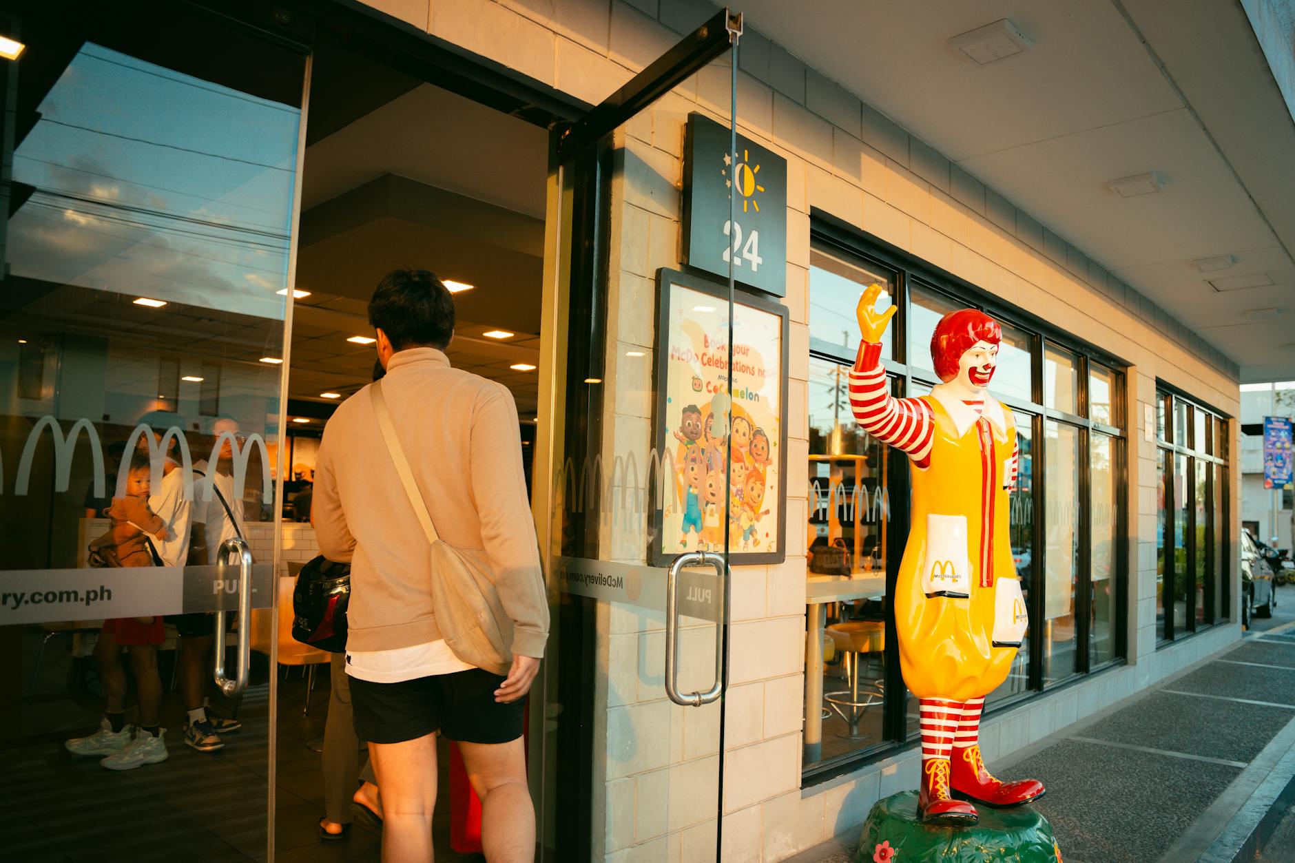 A man in casual attire enters a McDonald's restaurant, past a Ronald McDonald statue, during daylight. - healthiest mcdonald's breakfast