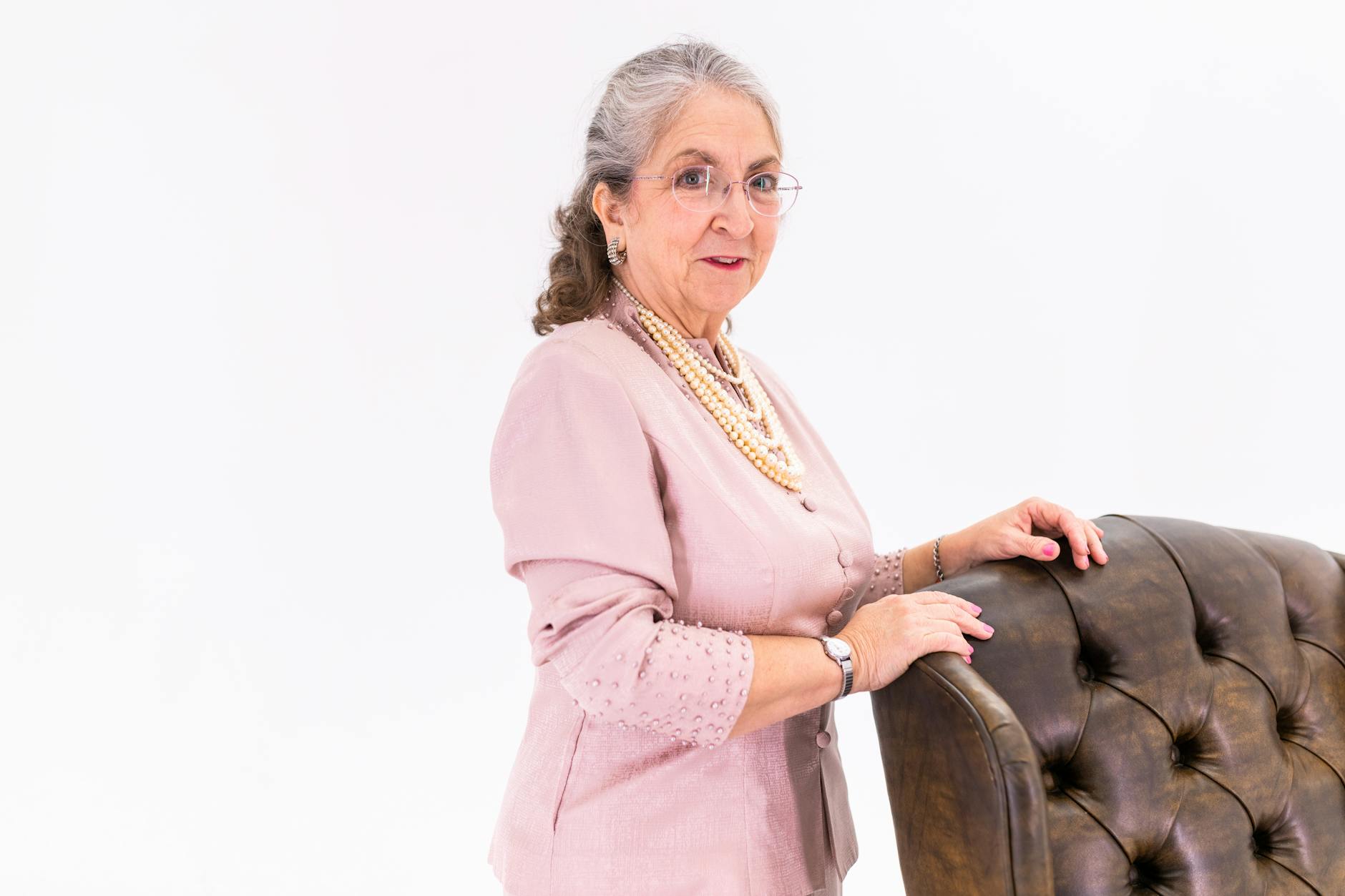 Stylish elderly woman in pink jacket standing beside an elegant chair indoors. - healthy aging tips seniors