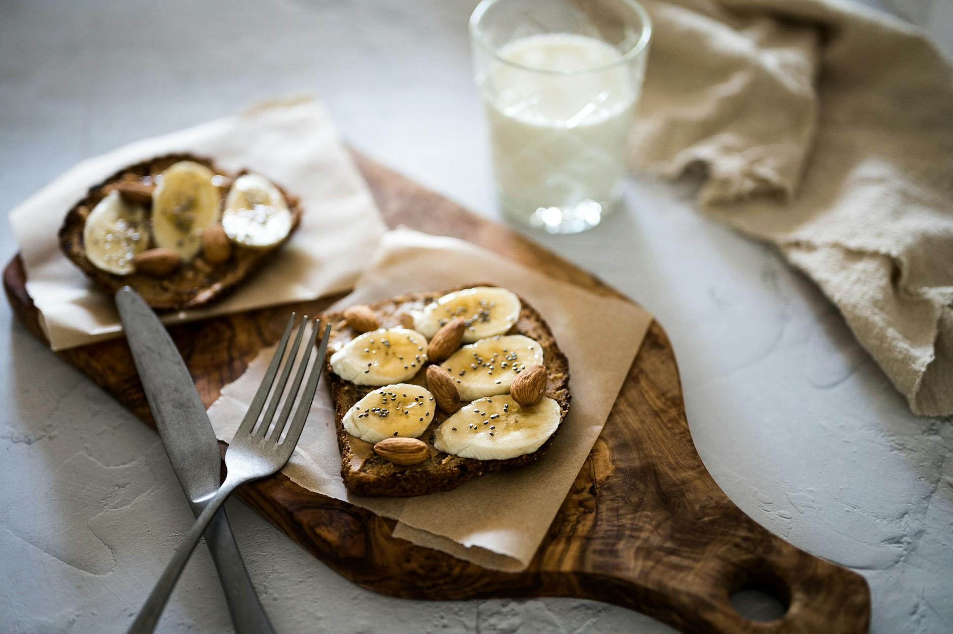 Delicious sliced banana and almond toast on rustic wooden board with milk glass, perfect for breakfast. - healthy breakfast meal prep