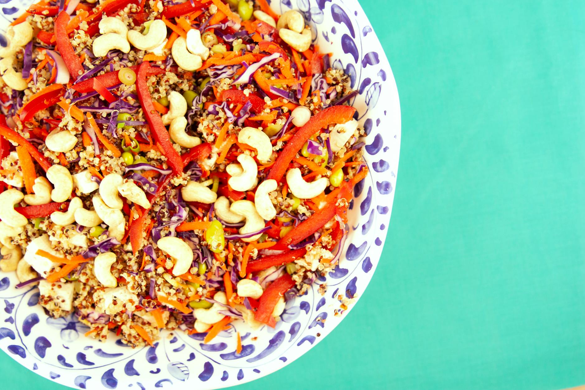 Colorful quinoa salad with cashews, peppers, and cabbage in a decorative bowl on a turquoise background. - healthy dinner recipes