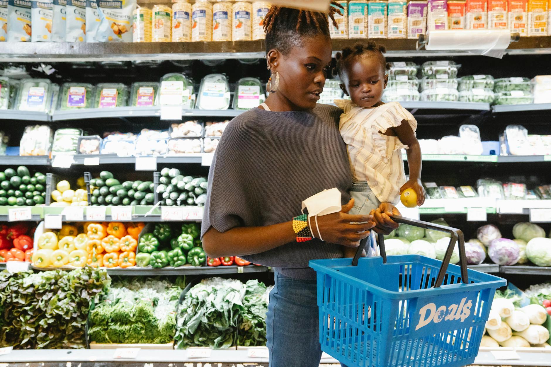 A mother carries her child while shopping in the supermarket's fresh produce section. - healthy food list