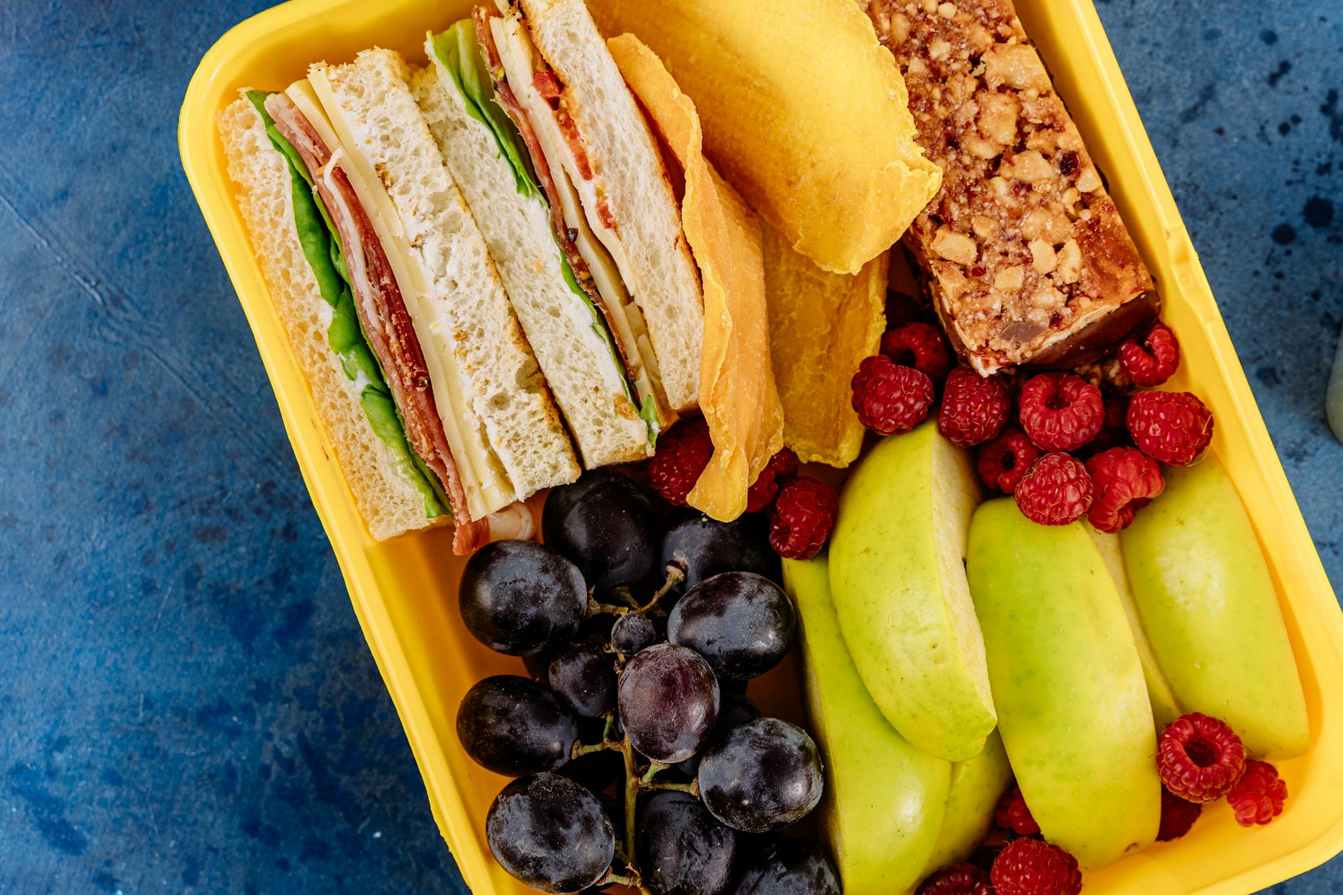 Vibrant lunchbox containing a sandwich, fresh fruits, and a snack bar, ideal for healthy meals. - healthy work lunch ideas