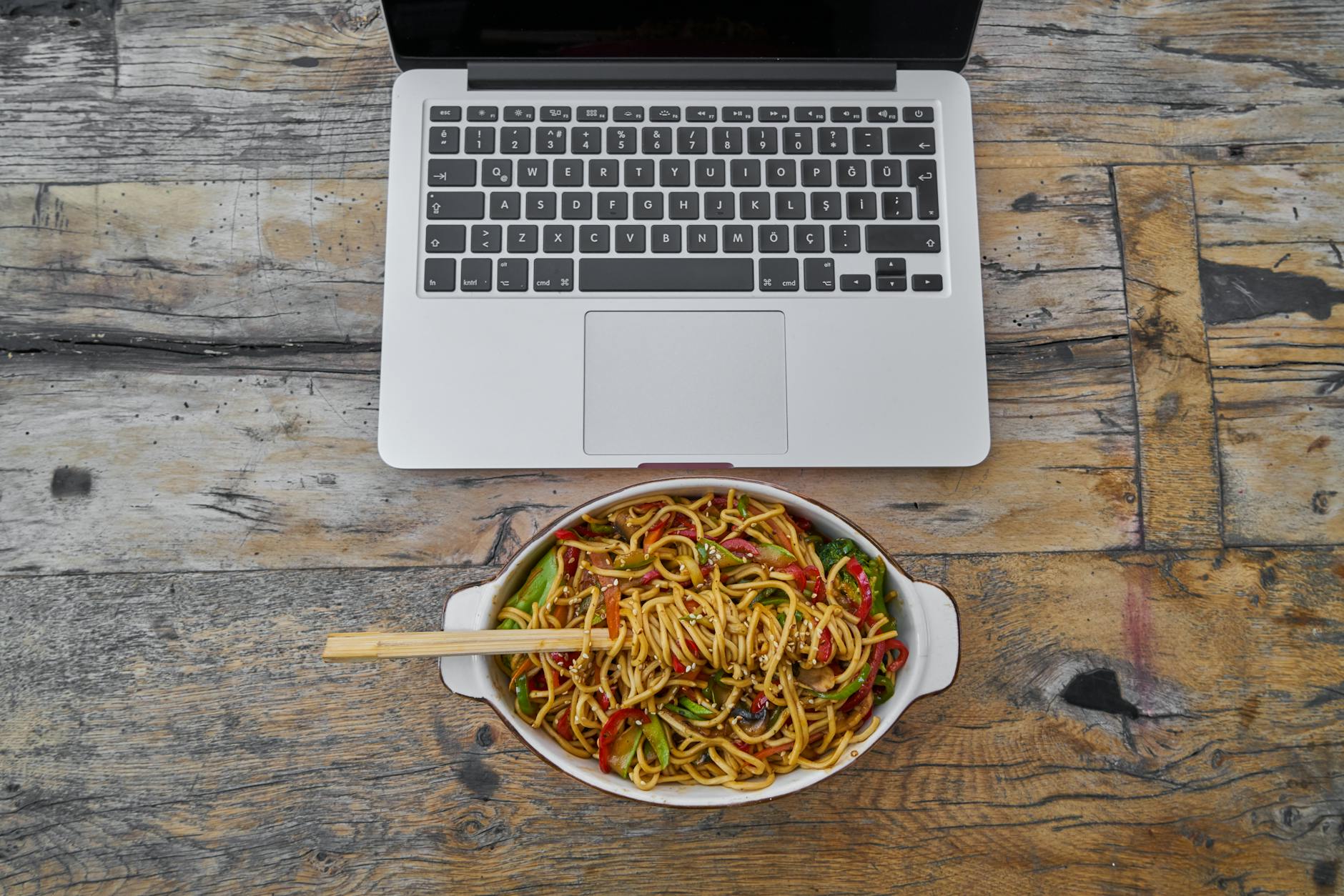Overhead view of laptop and noodle bowl on rustic wooden table, perfect blend of food and technology. - healthy work lunch ideas