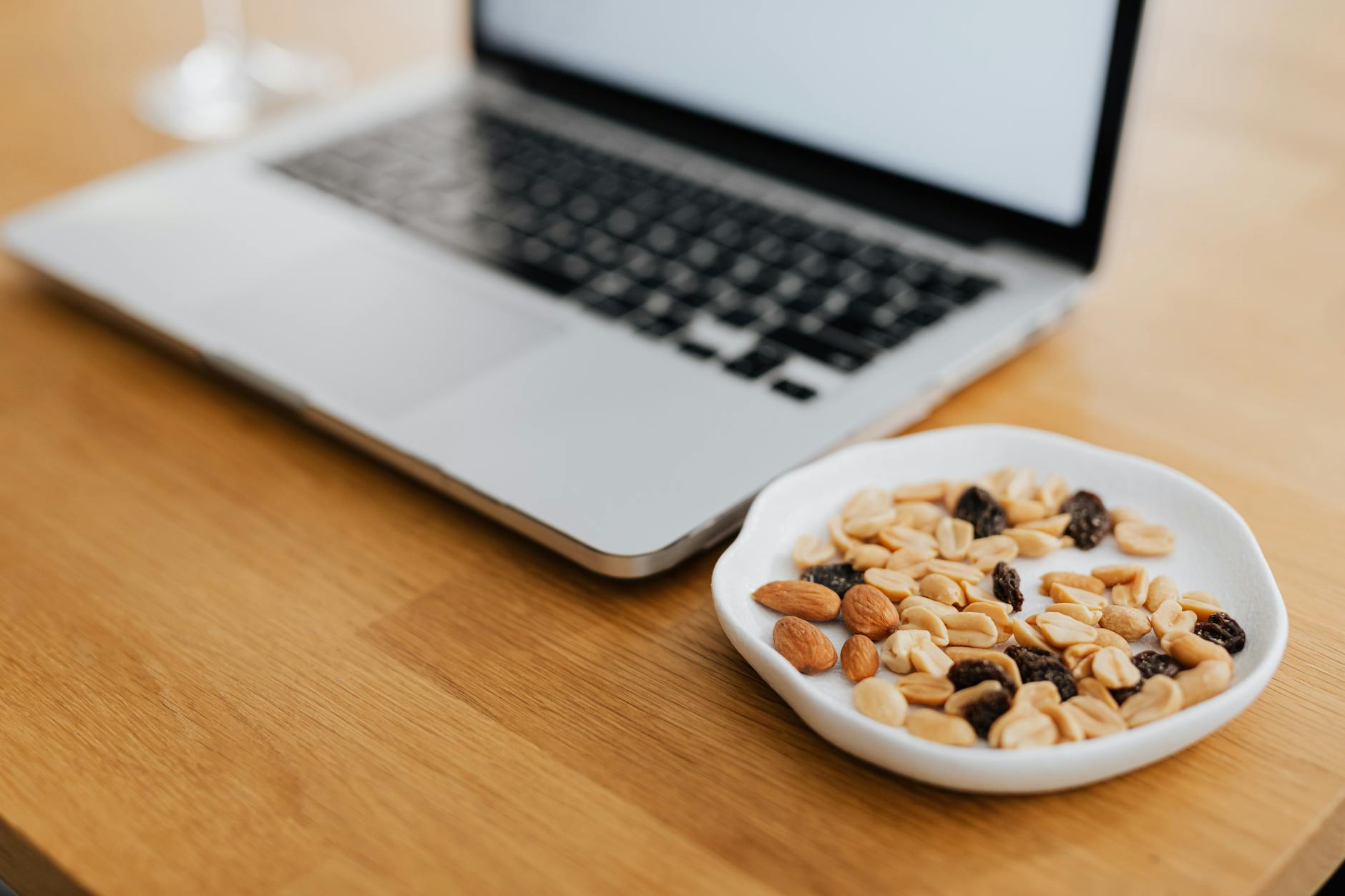 A plate of mixed nuts beside a laptop on a wooden desk, perfect for remote work inspiration. - healthy work snacks