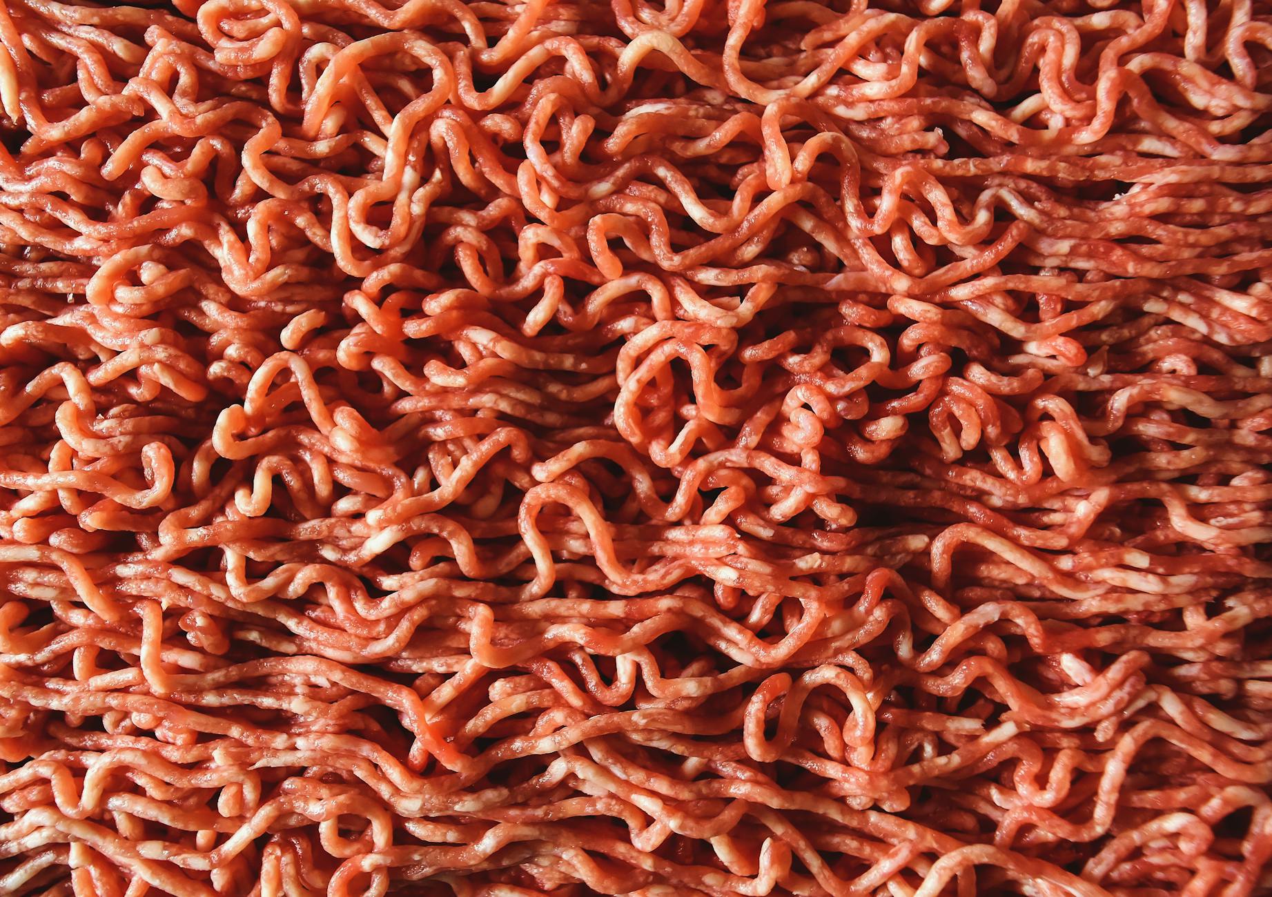 Detailed close-up image of raw, red ground beef with visible strands. - high protein foods
