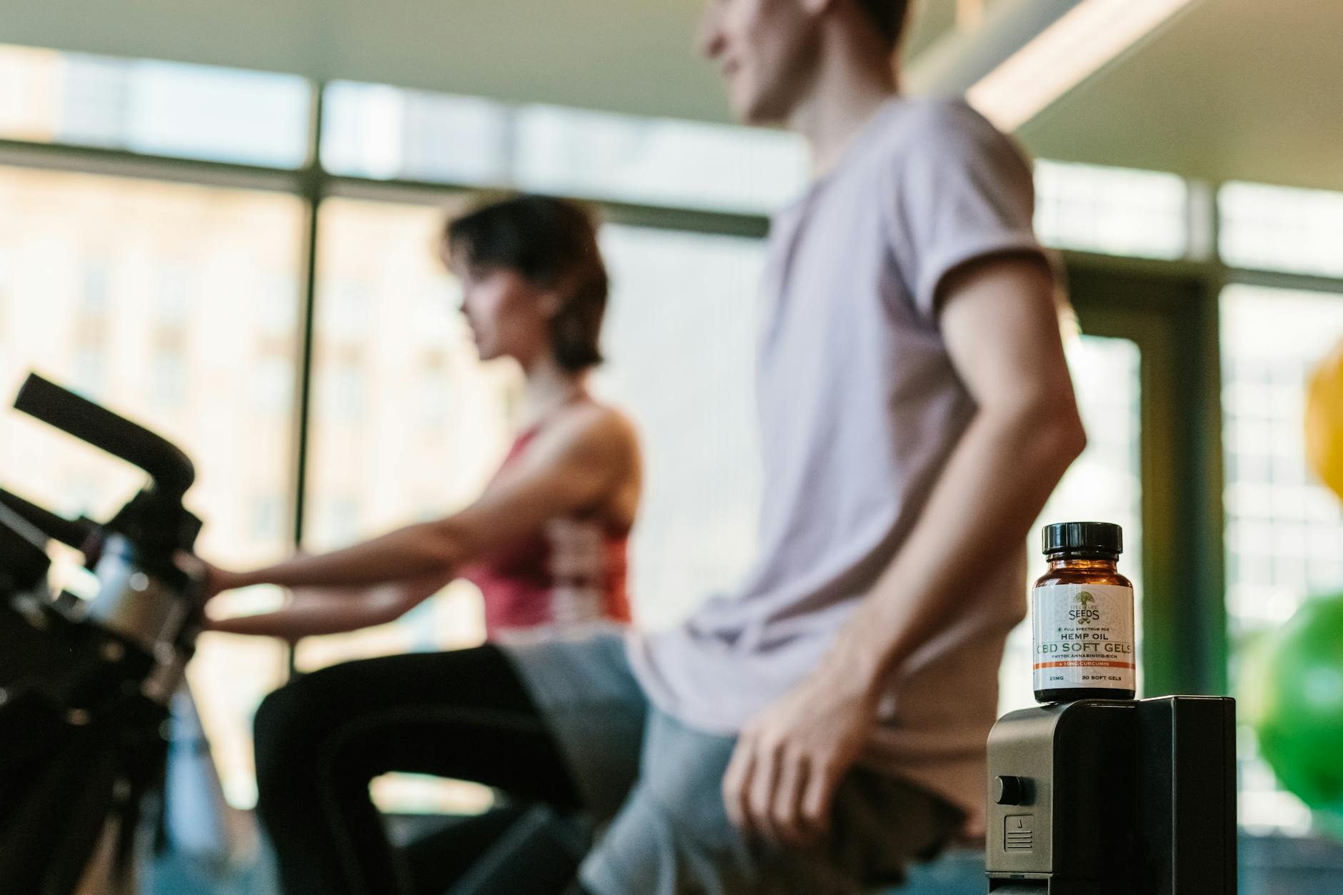 CBD gel bottle in gym with exercising adults, suggesting health benefits. - morning workout benefits