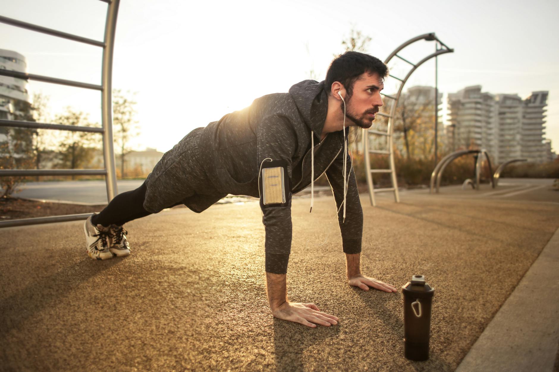 Adult man doing push-ups outdoors with earphones during sunrise, showcasing fitness and healthy lifestyle. - morning workout for men