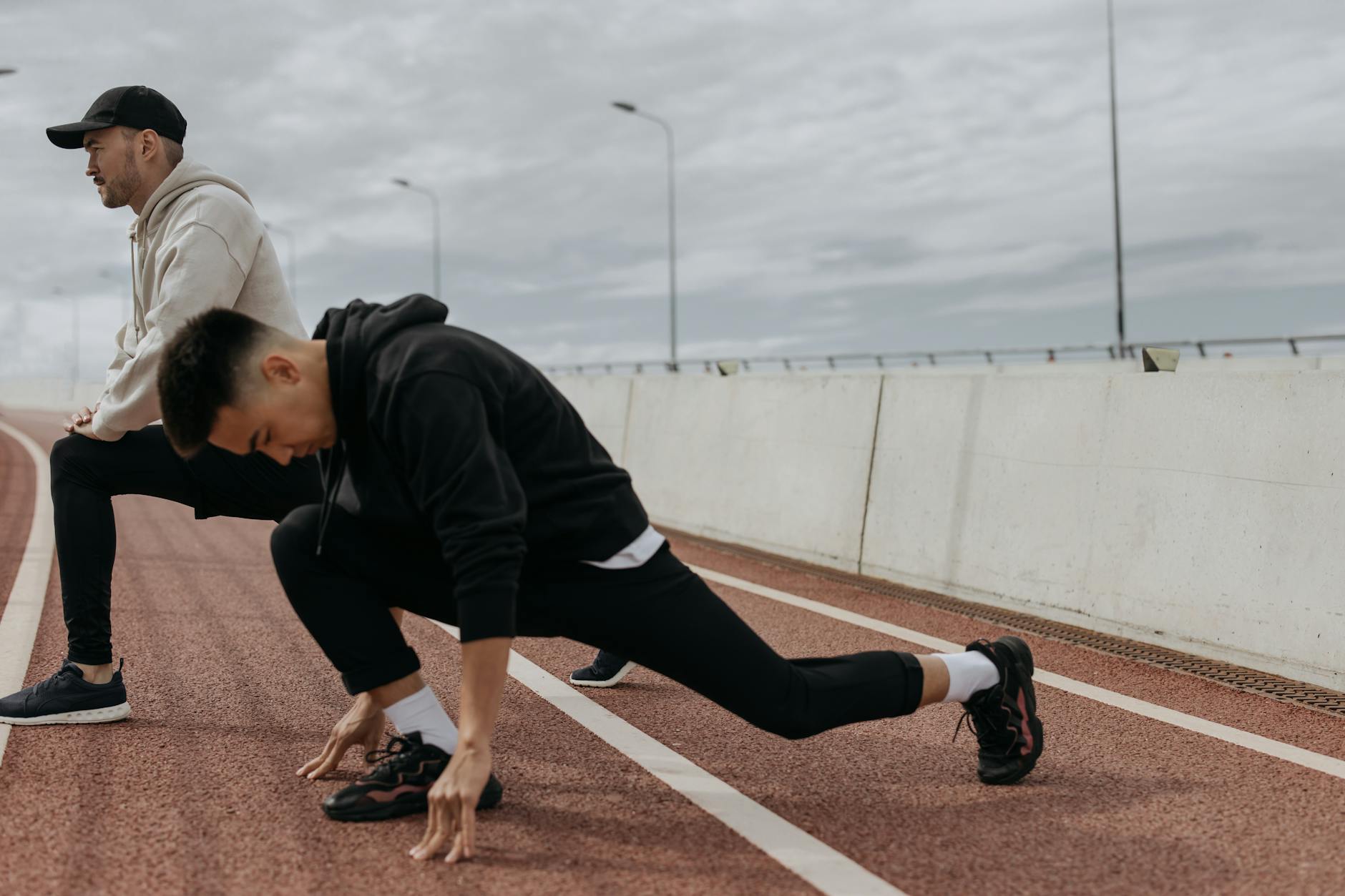 Two men stretching on an outdoor track, preparing for a workout session. - morning workout for men