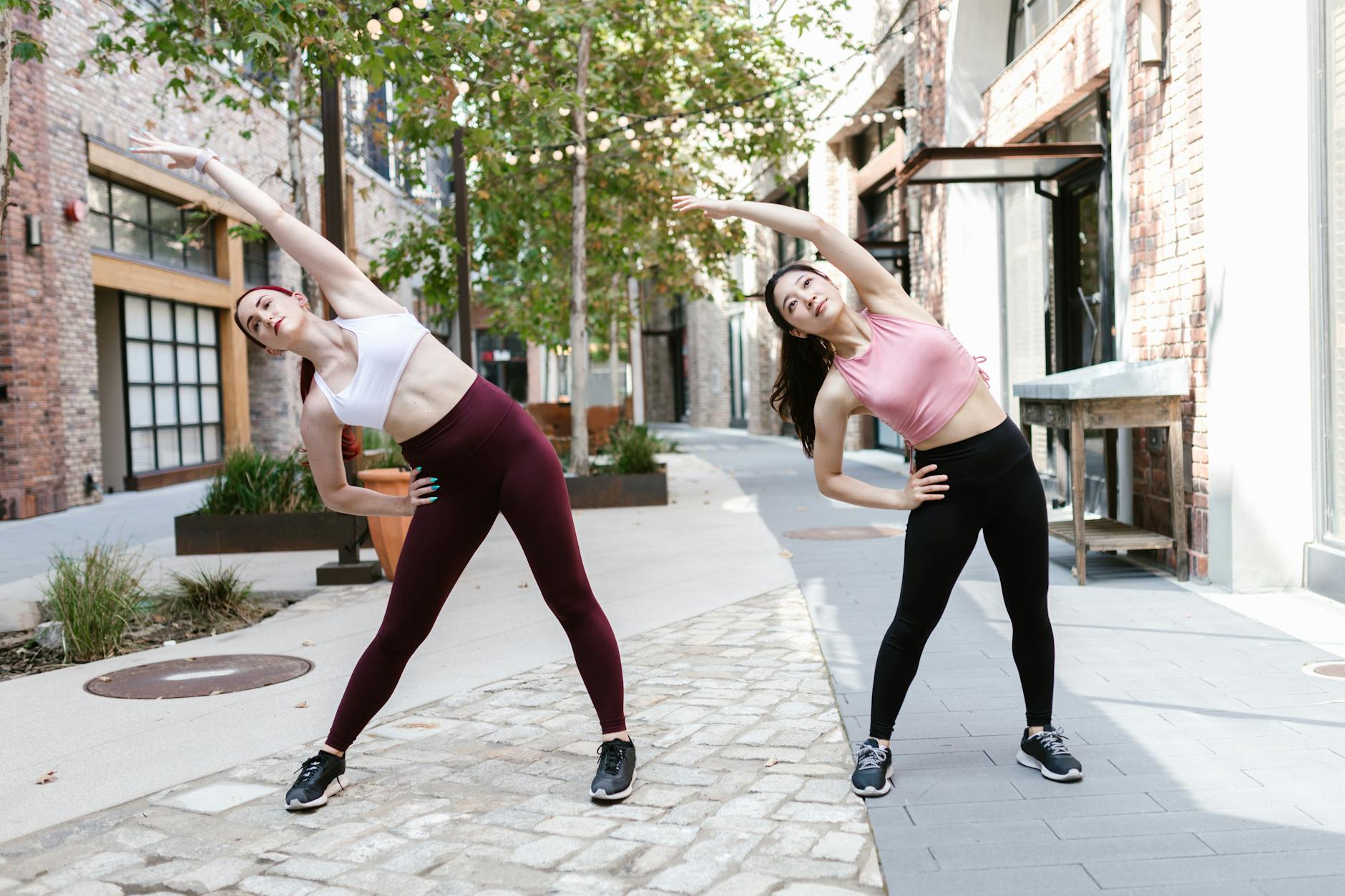 Two women perform stretching exercises outdoors in an urban setting, promoting a healthy lifestyle. - morning workouts for women
