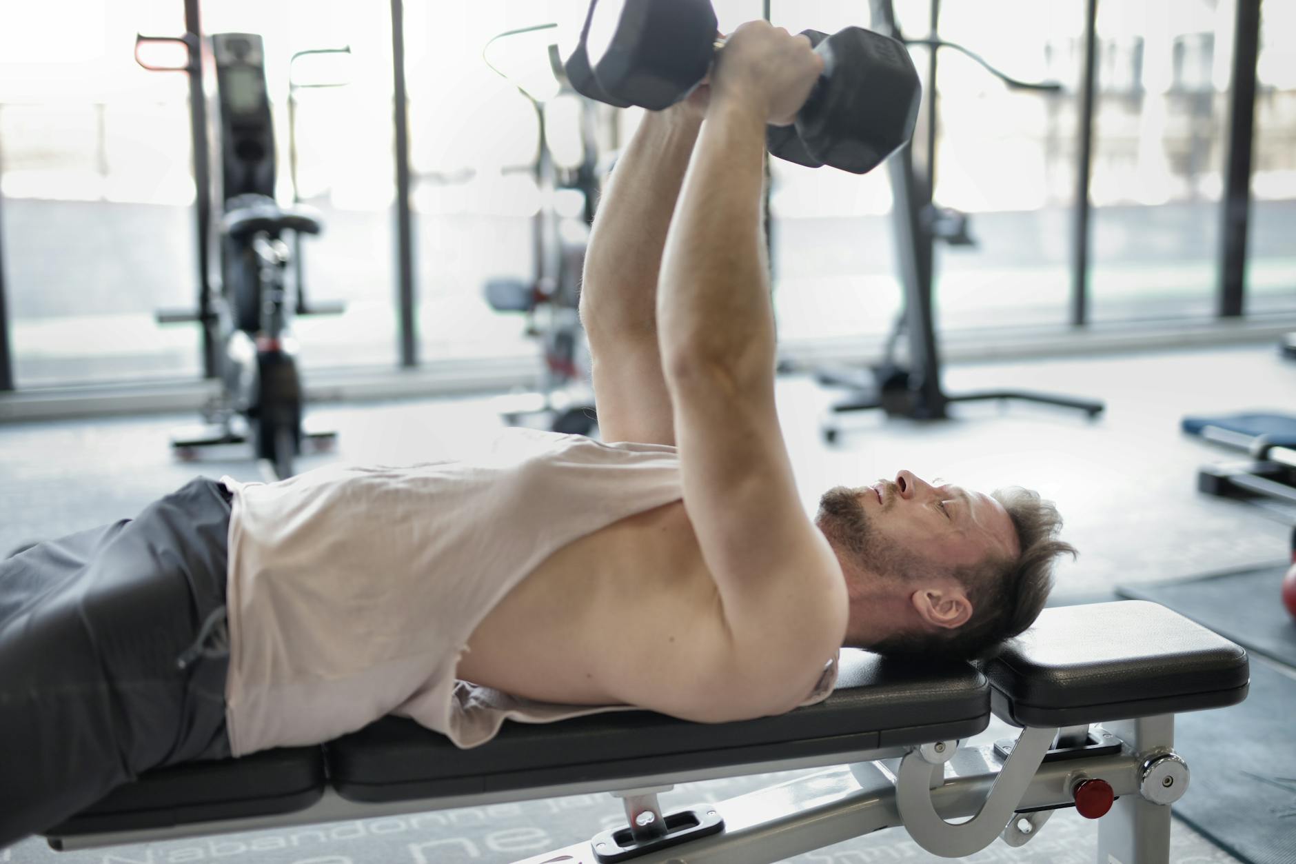 Active man engaged in strength training with dumbbells in a modern gym setting. - muscle building workout plan