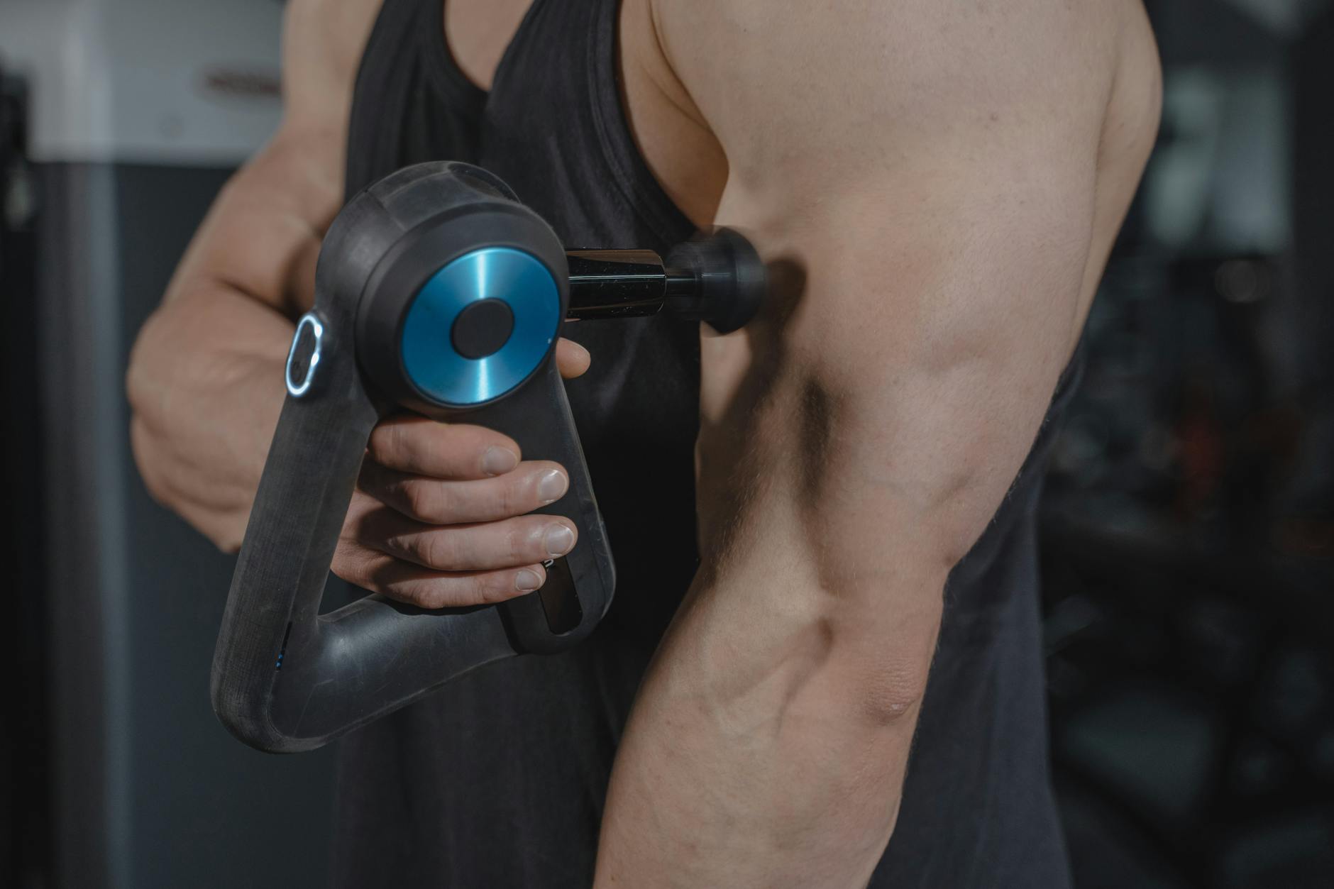 Close-up of a man using a massage gun for muscle relaxation on his arm. - muscle recovery after workout