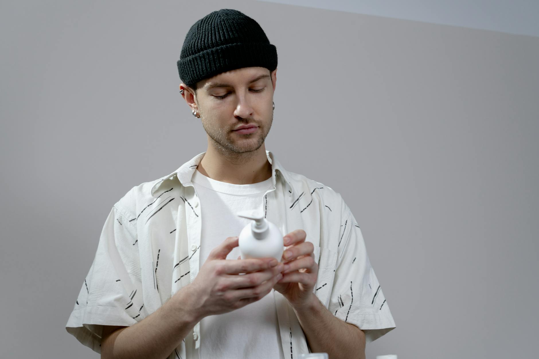 A young man examines a shampoo bottle in a modern indoor setting, wearing casual attire. - just natural skincare reviews