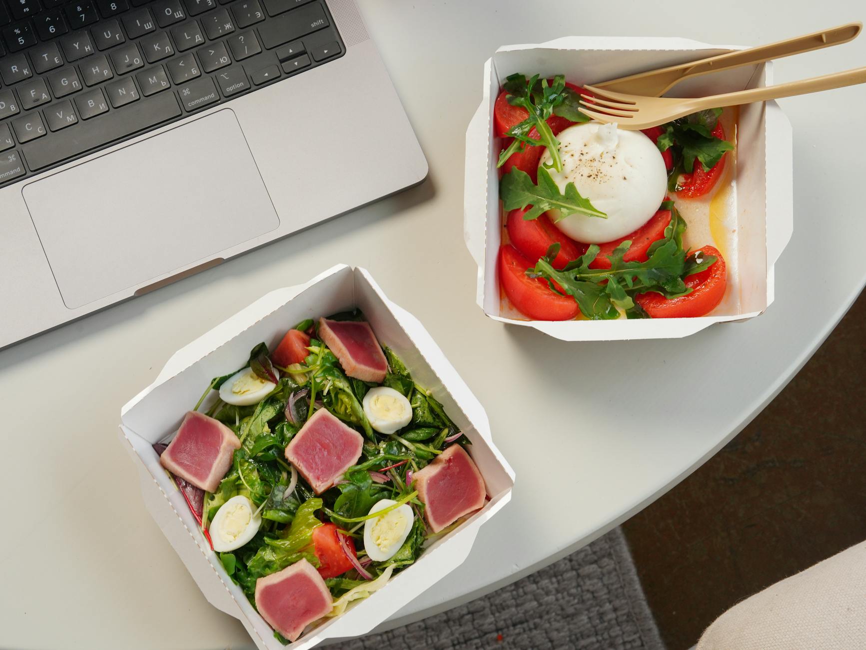 Top view of a desk setup with two fresh salads and a laptop, ideal for a healthy office lunch. - quick healthy lunches