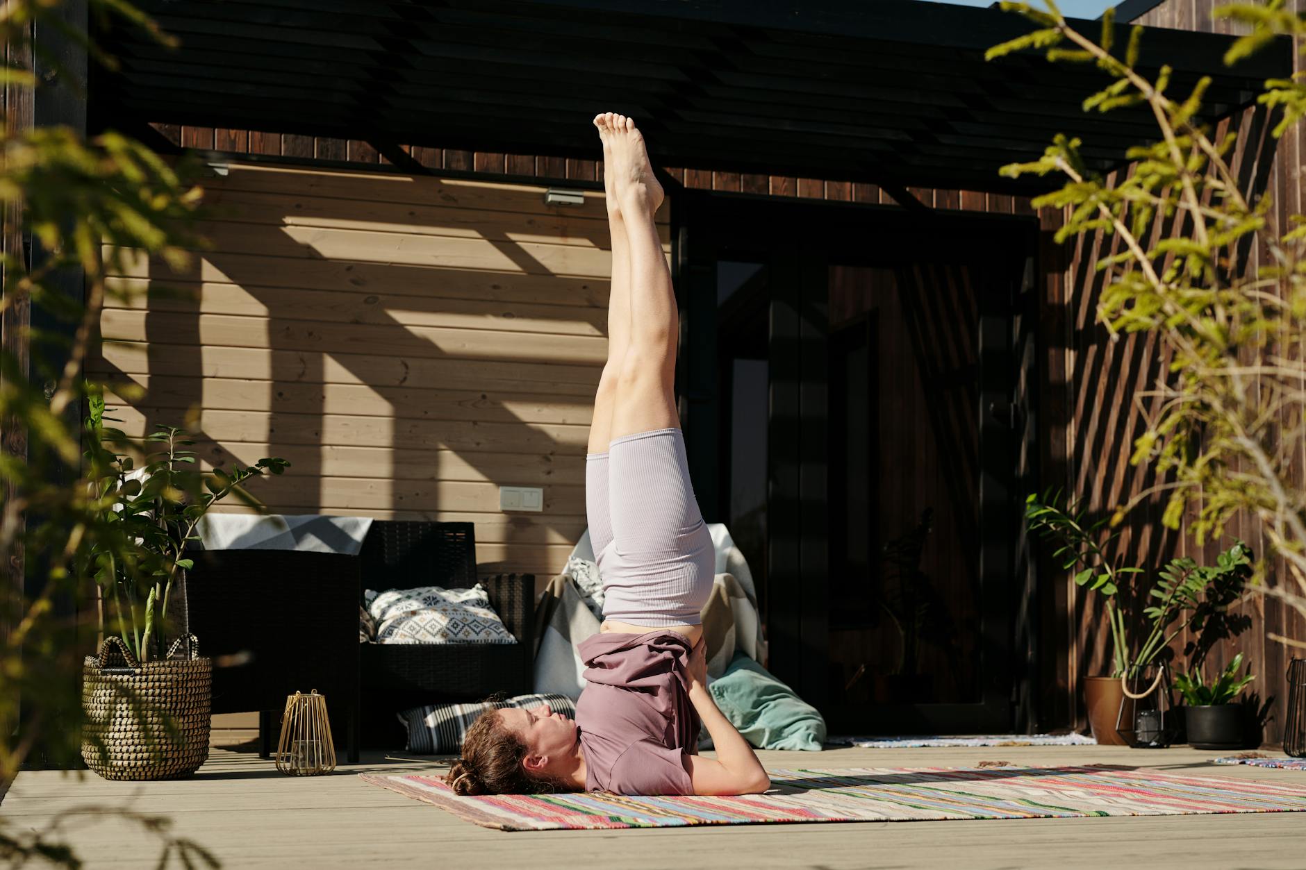 A woman performing a shoulder stand yoga pose on a sunny outdoor patio, enhancing flexibility and mindfulness. - shoulder flexibility exercises