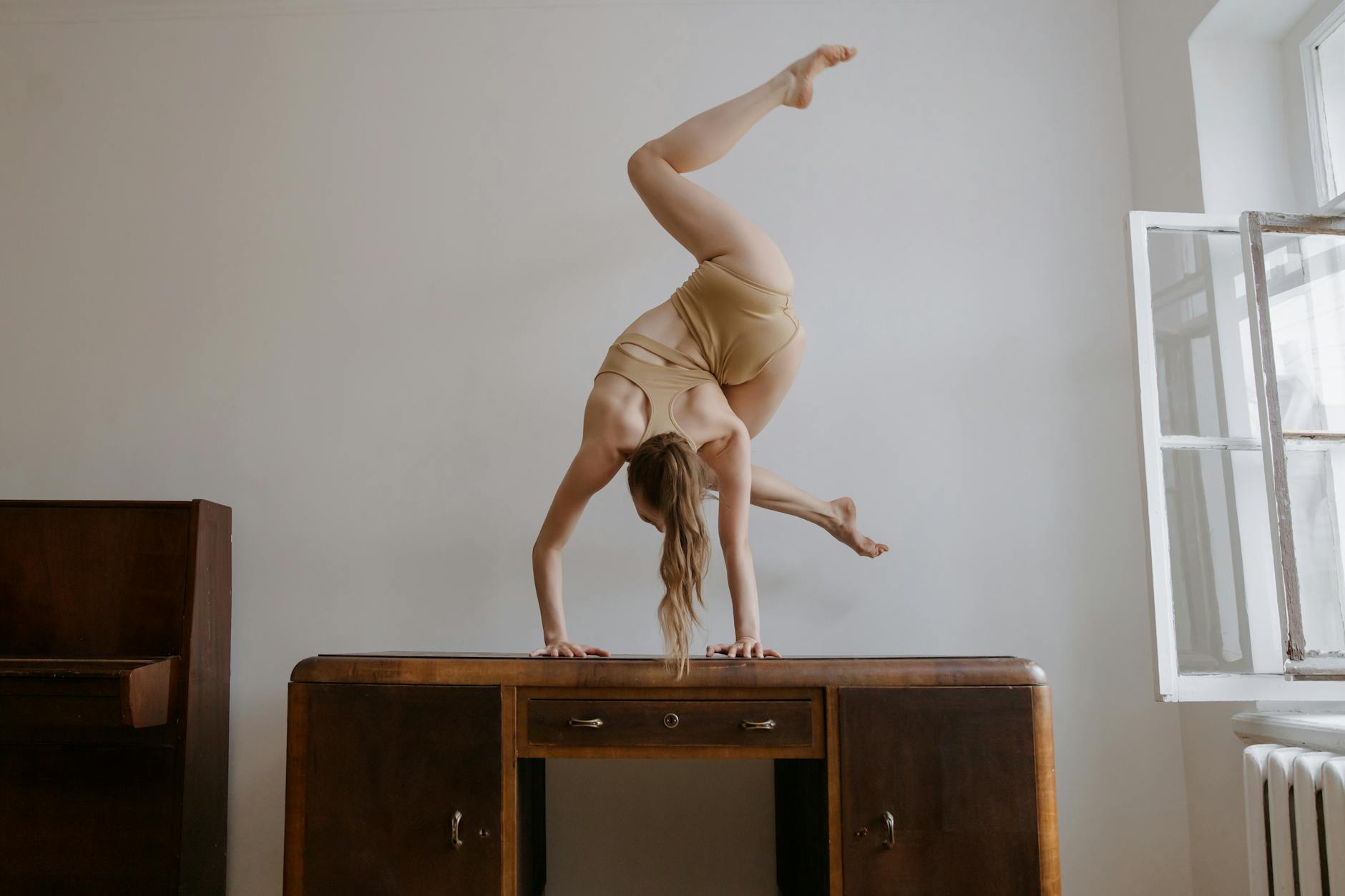 A female athlete showcases flexibility with an artistic handstand on a desk indoors. - standing desk exercises
