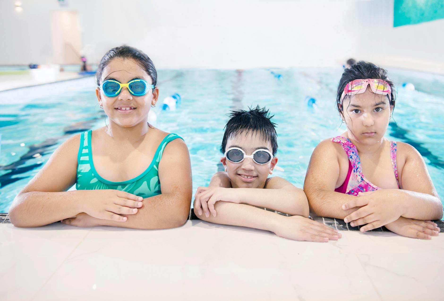 Three smiling children in swimwear enjoying a swim at an indoor pool. Perfect for lifestyle and leisure themes. - swimming benefits for children