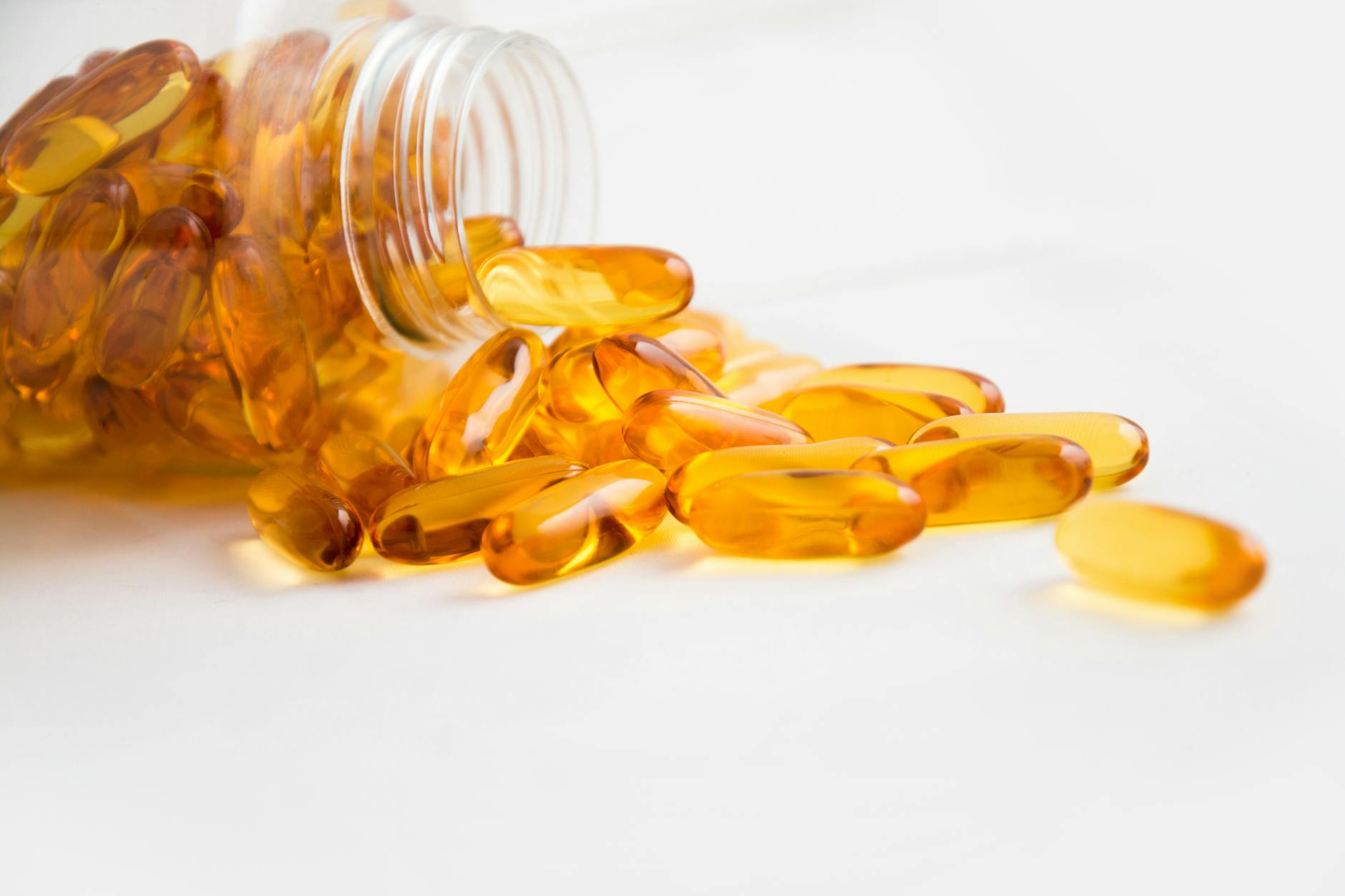 Close-up of fish oil capsules spilling from a bottle on white background. - swimming benefits for health