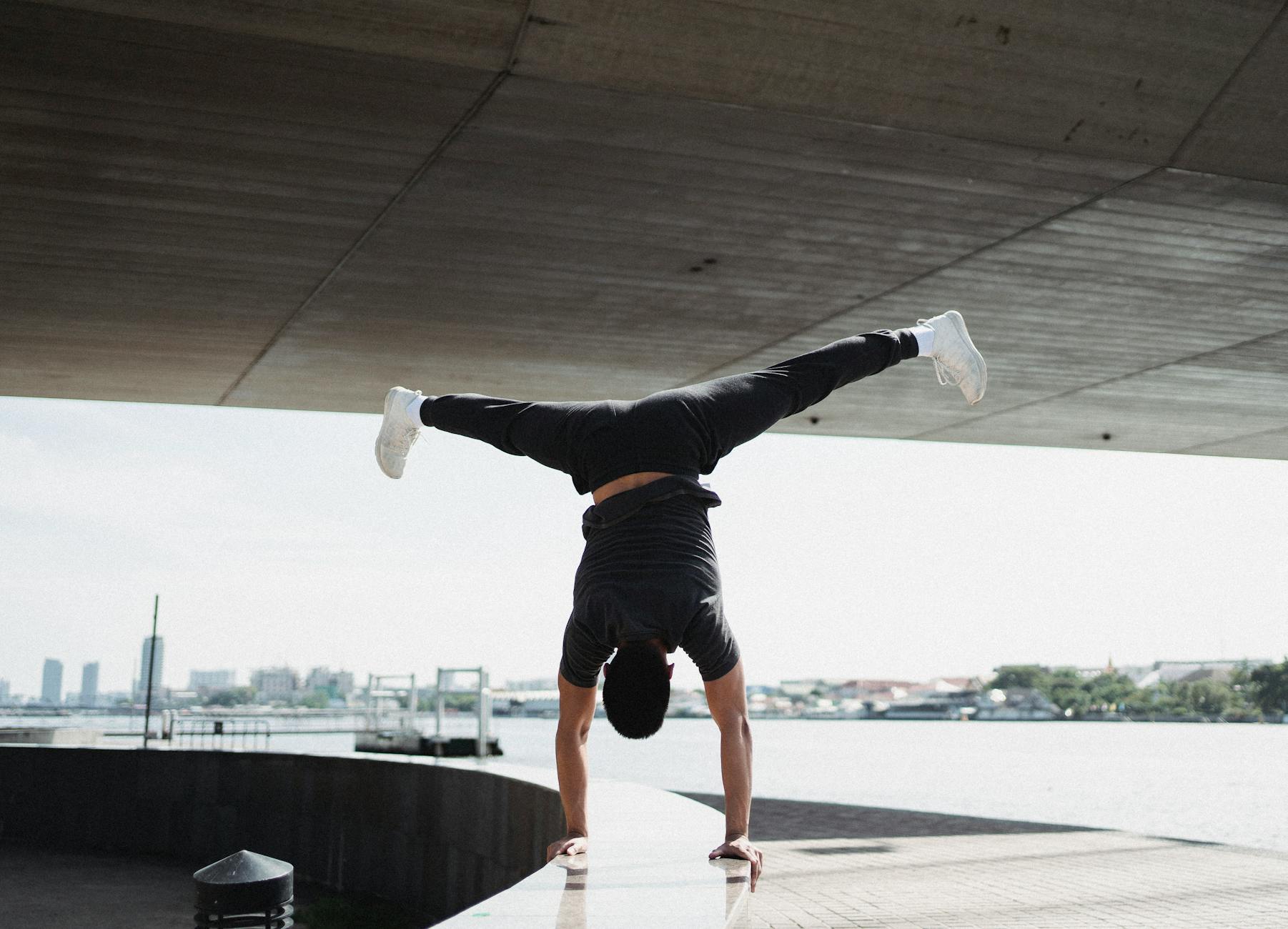 Back view full body strong sportsman performing handstand and split in air while working out on sunny city embankment - upper back posture exercises
