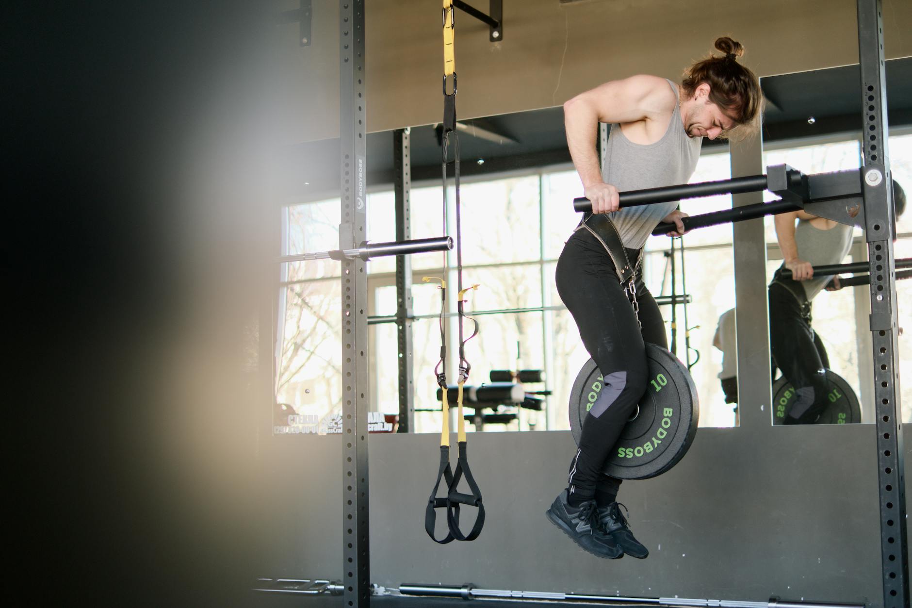 Fit man performing weighted pull-ups in a gym setting, showing strength and determination. - 30 day fitness challenge