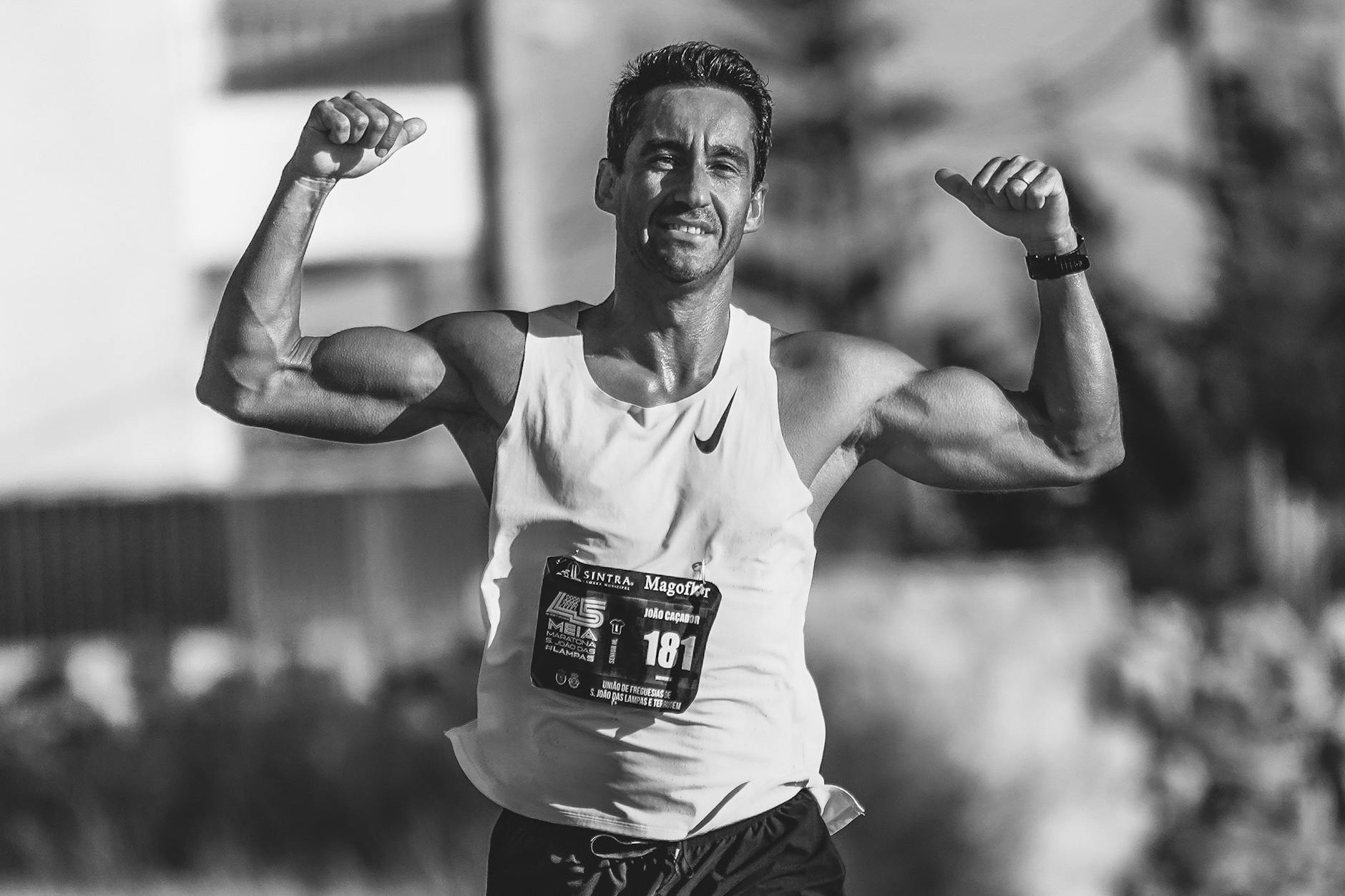 Black and white photo of a victorious male runner celebrating with raised arms on a track. - 30 day fitness challenge