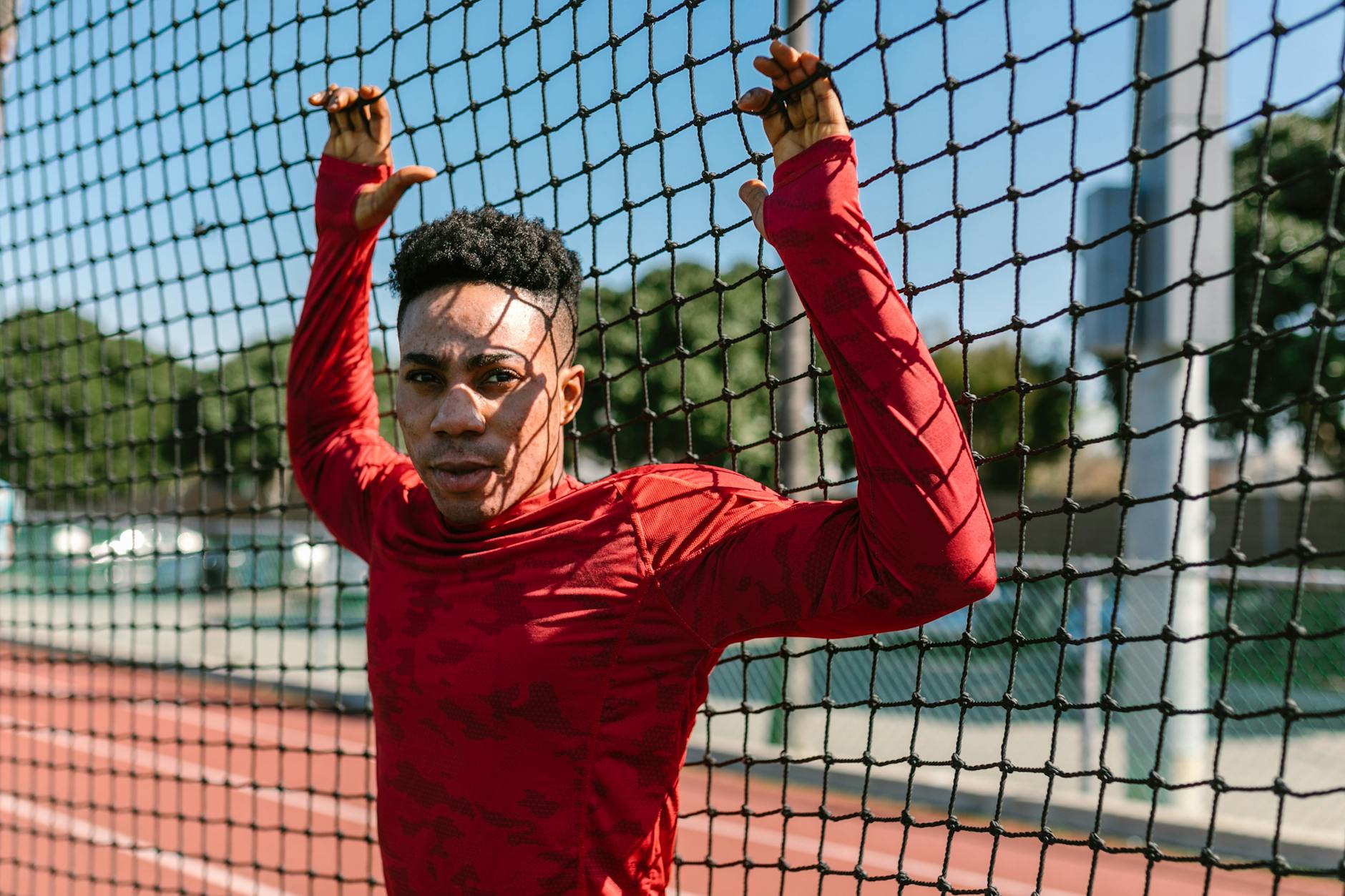 An athlete in red sportswear leans on a net on an outdoor track. - abs workout