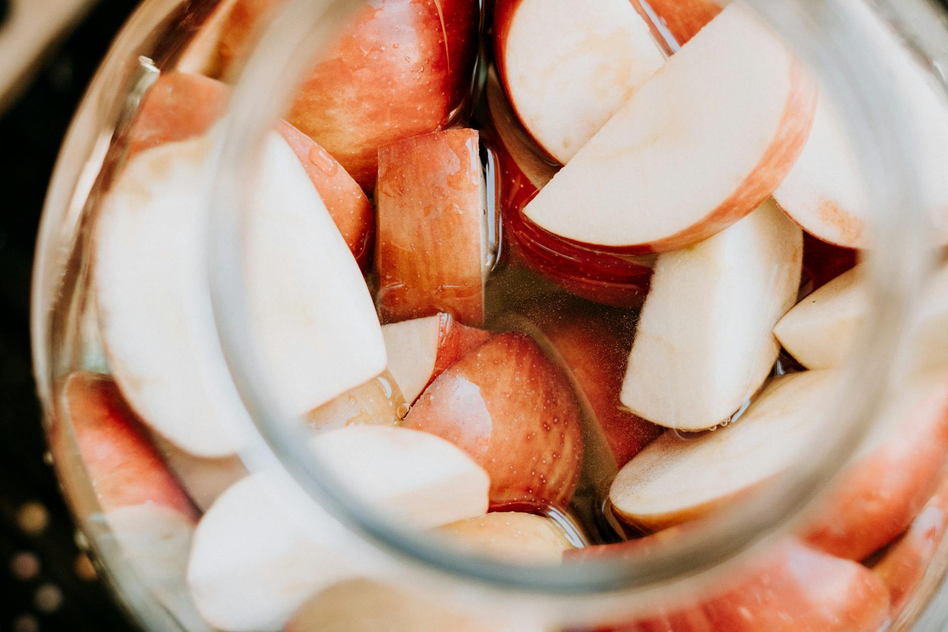 Close-up of fresh apple slices submerged in liquid, seen through a glass jar. - apple detox water