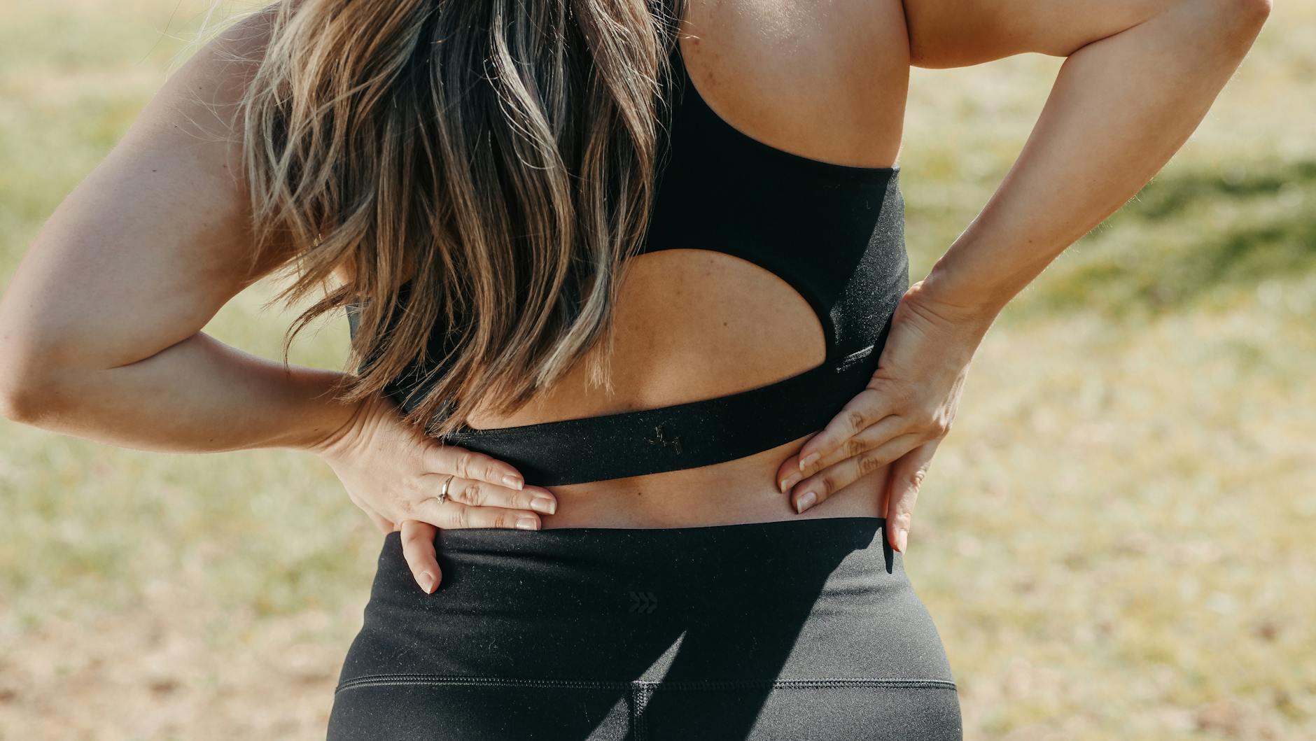 Close-up of a woman holding her back, suggesting back pain outdoors. - back pain stretches