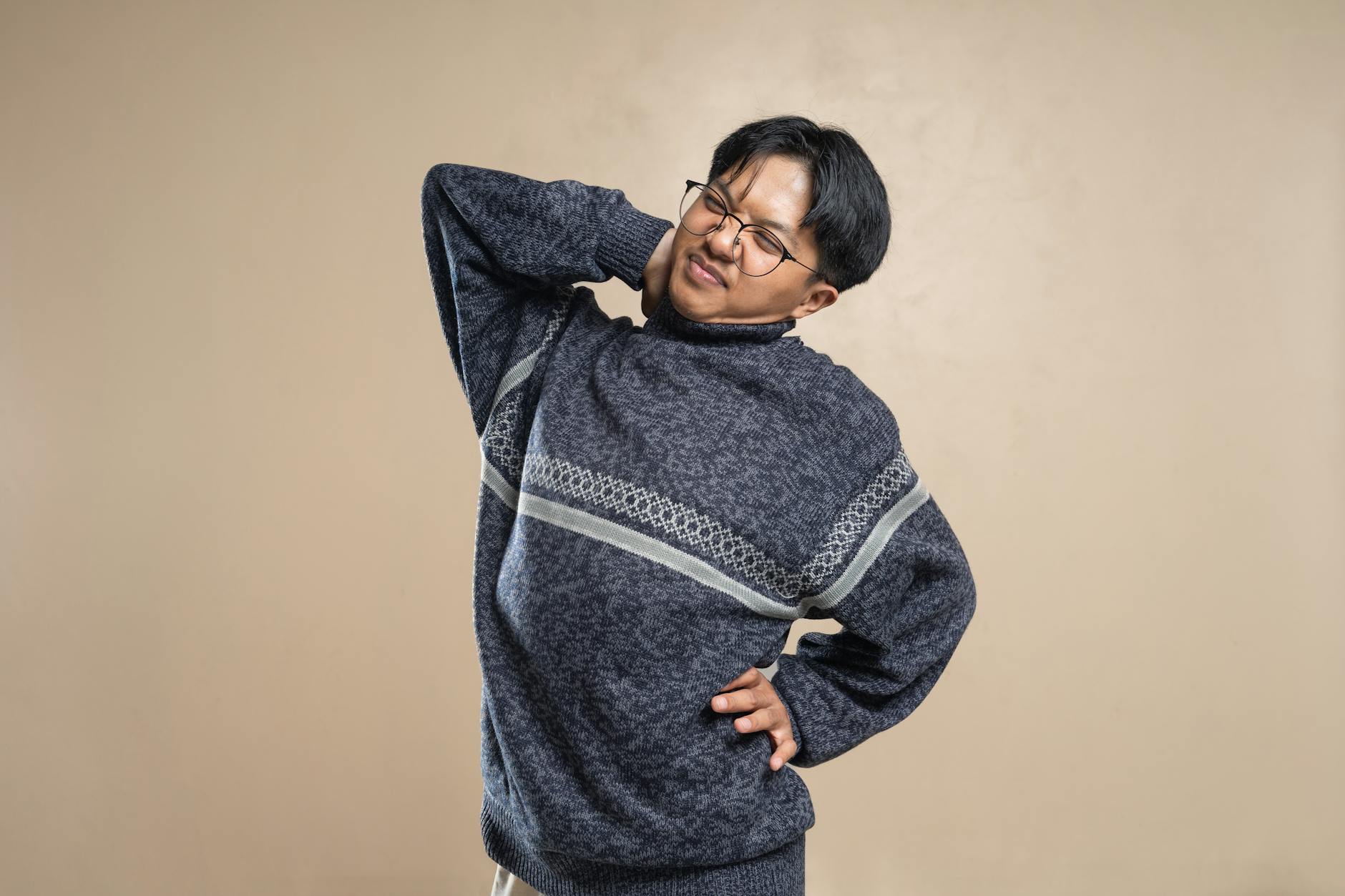 Asian man wearing eyeglasses and sweater stretching indoors, feeling body pain. - back pain stretches