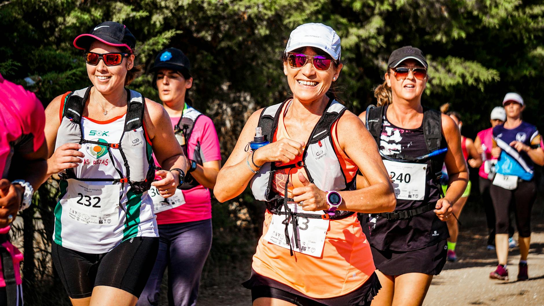 A group of smiling women participating in an outdoor marathon run with race numbers. - beginner running plan
