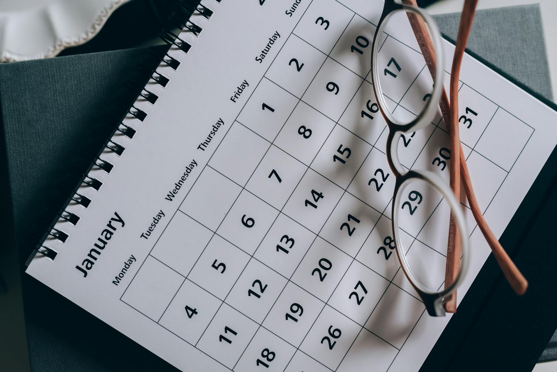 A close-up of a January calendar with eyeglasses on a table, emphasizing planning and organization. - beginner running schedule