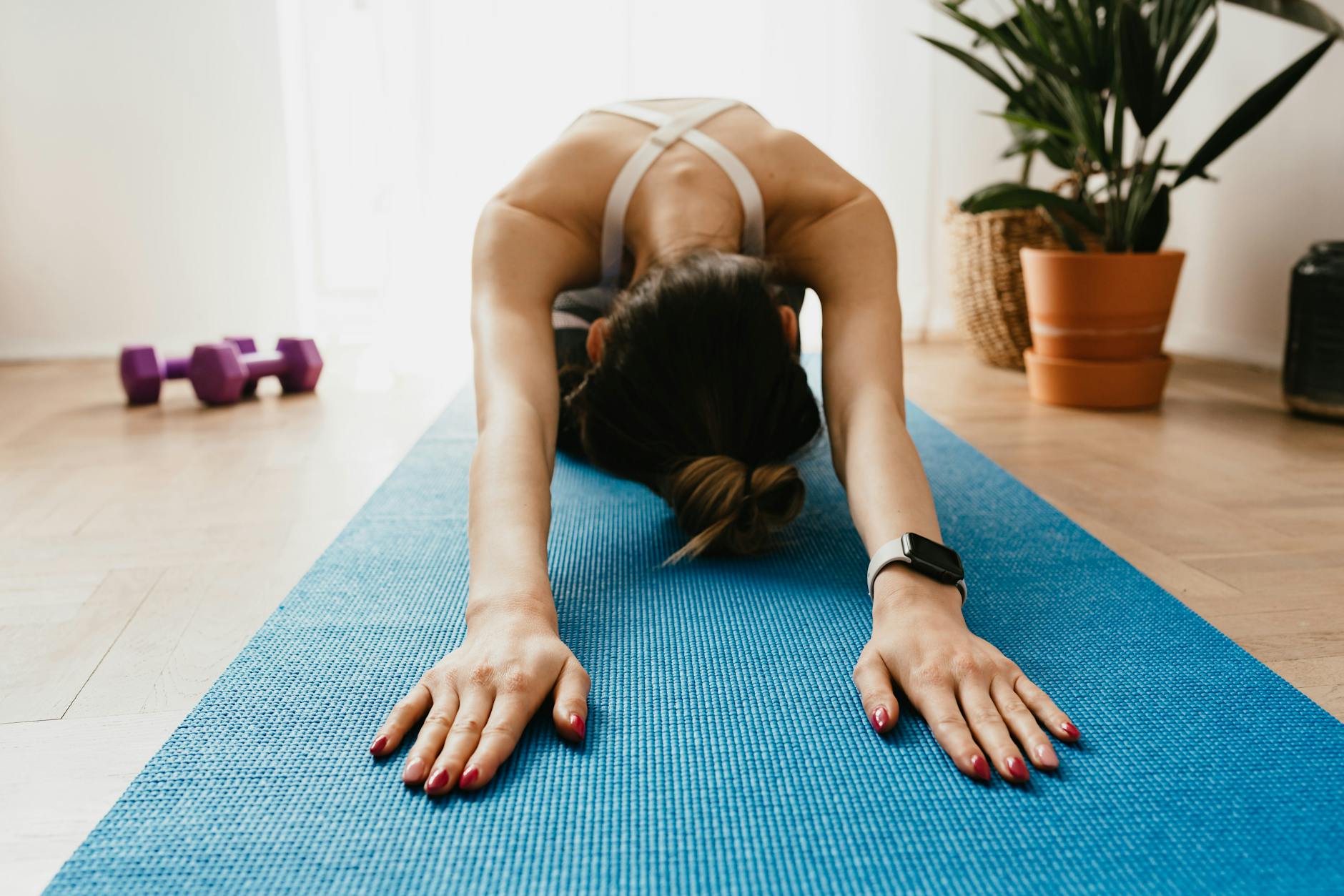 Woman doing a child's pose on a blue yoga mat at home, promoting fitness and wellbeing. - beginner stretching routine