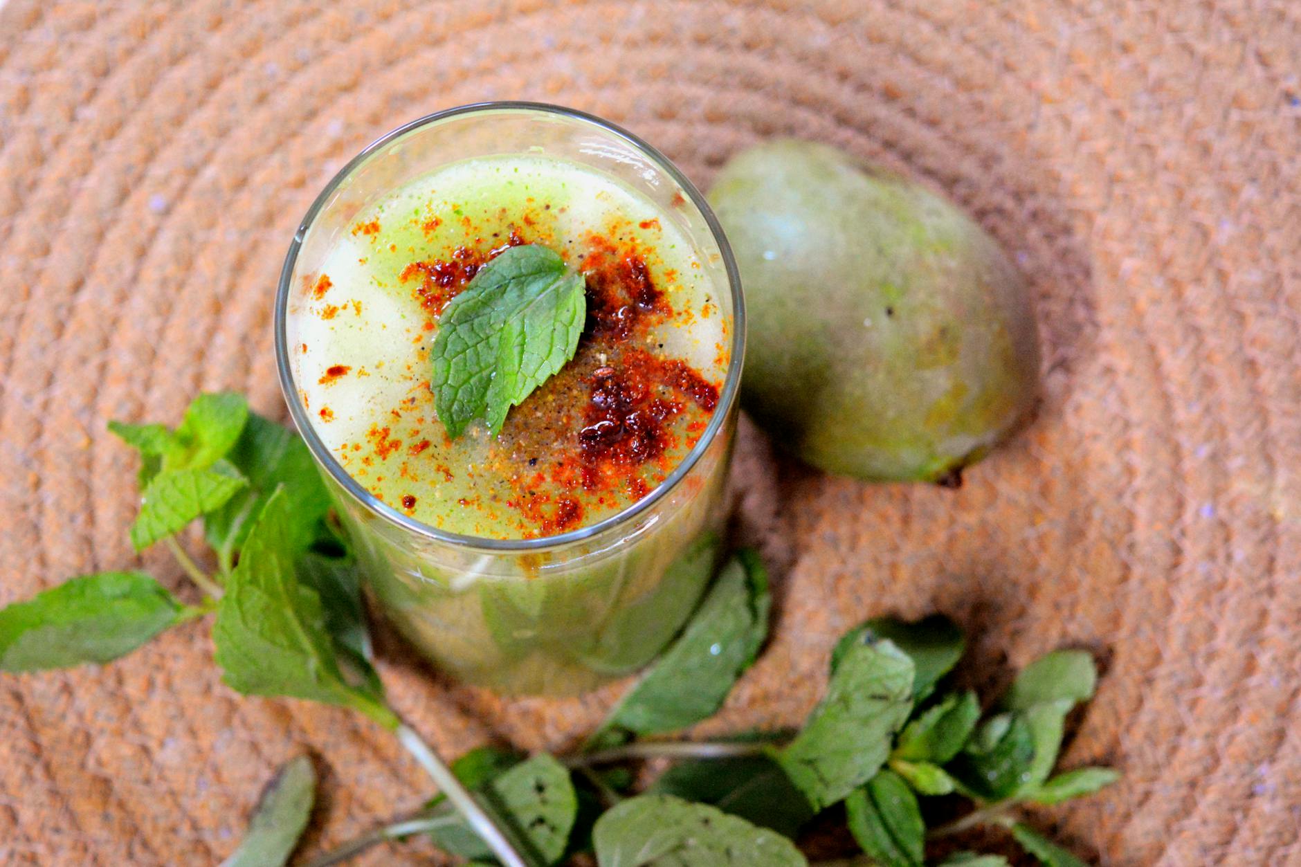 Top view of a refreshing glass of Aam Panna garnished with mint leaves and spices, placed on a woven mat. - best anti inflammatory foods