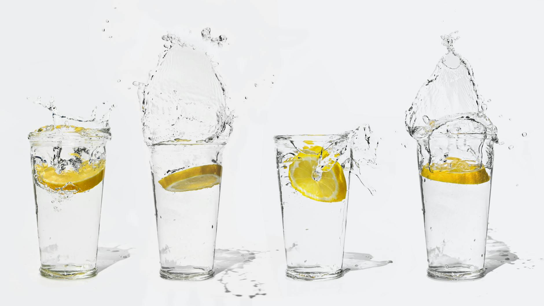 Four glasses with lemon slices creating splashes of water on a white background. - best detox water