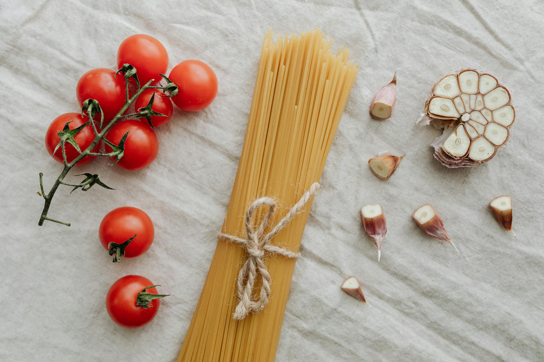 Flat lay of cherry tomatoes, garlic, and uncooked spaghetti on a neutral background. Ideal for food photography. - best mediterranean cookbook