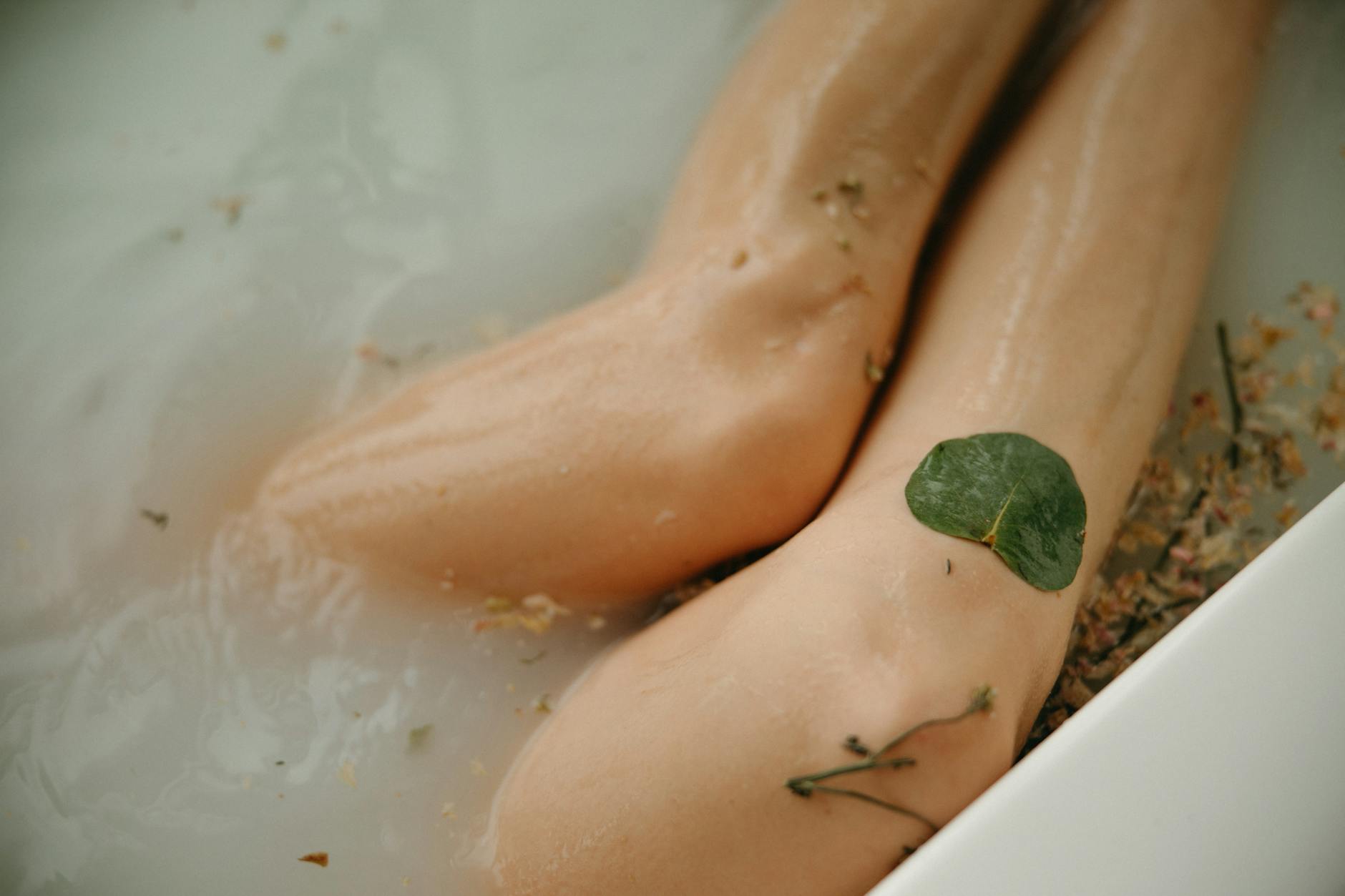 Close-up of legs in a soothing bath with a leaf and petals floating. - body detox cleanse