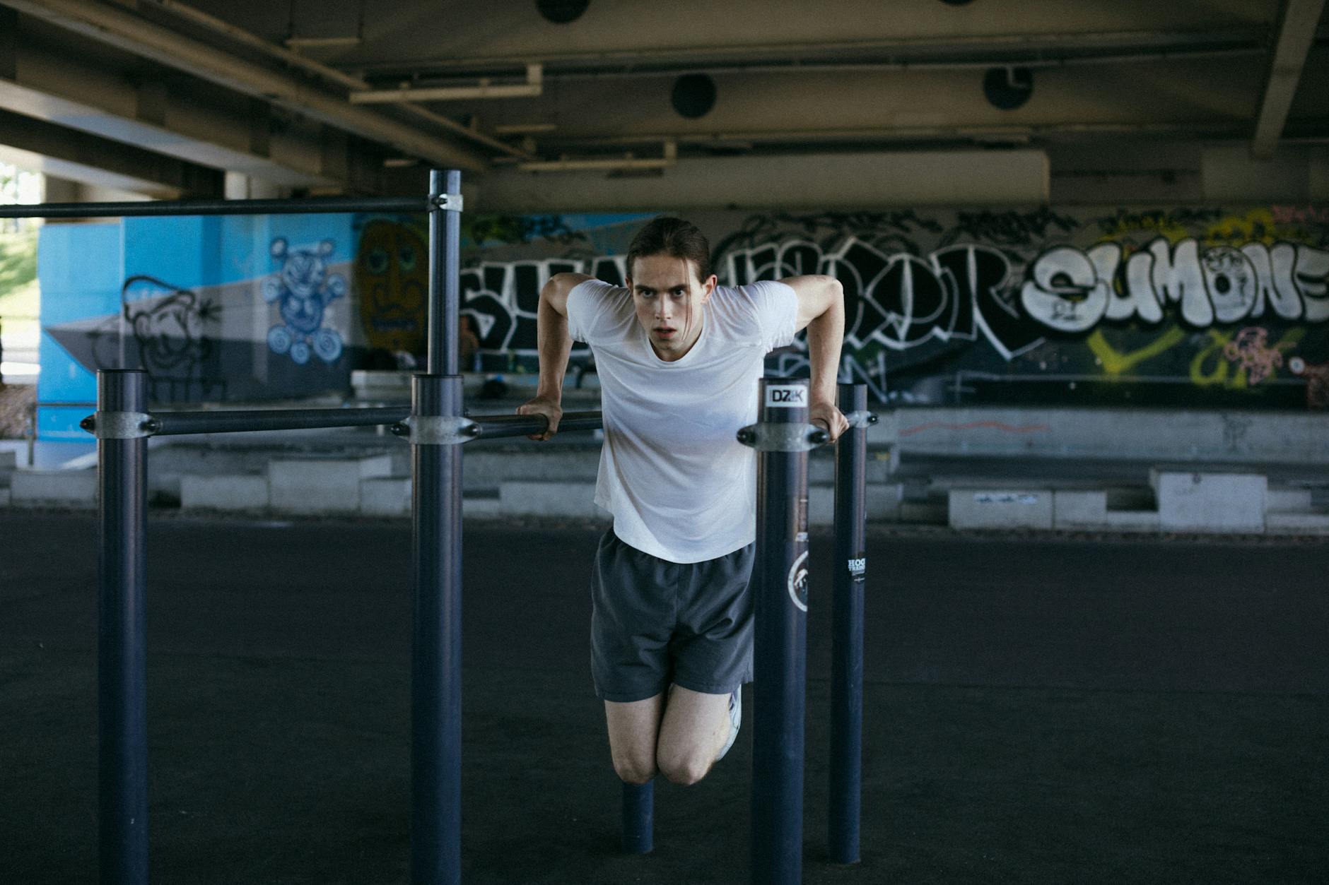 Athletic man in urban setting exercises on bars with vibrant graffiti background, showcasing flexibility. - bodyweight cardio