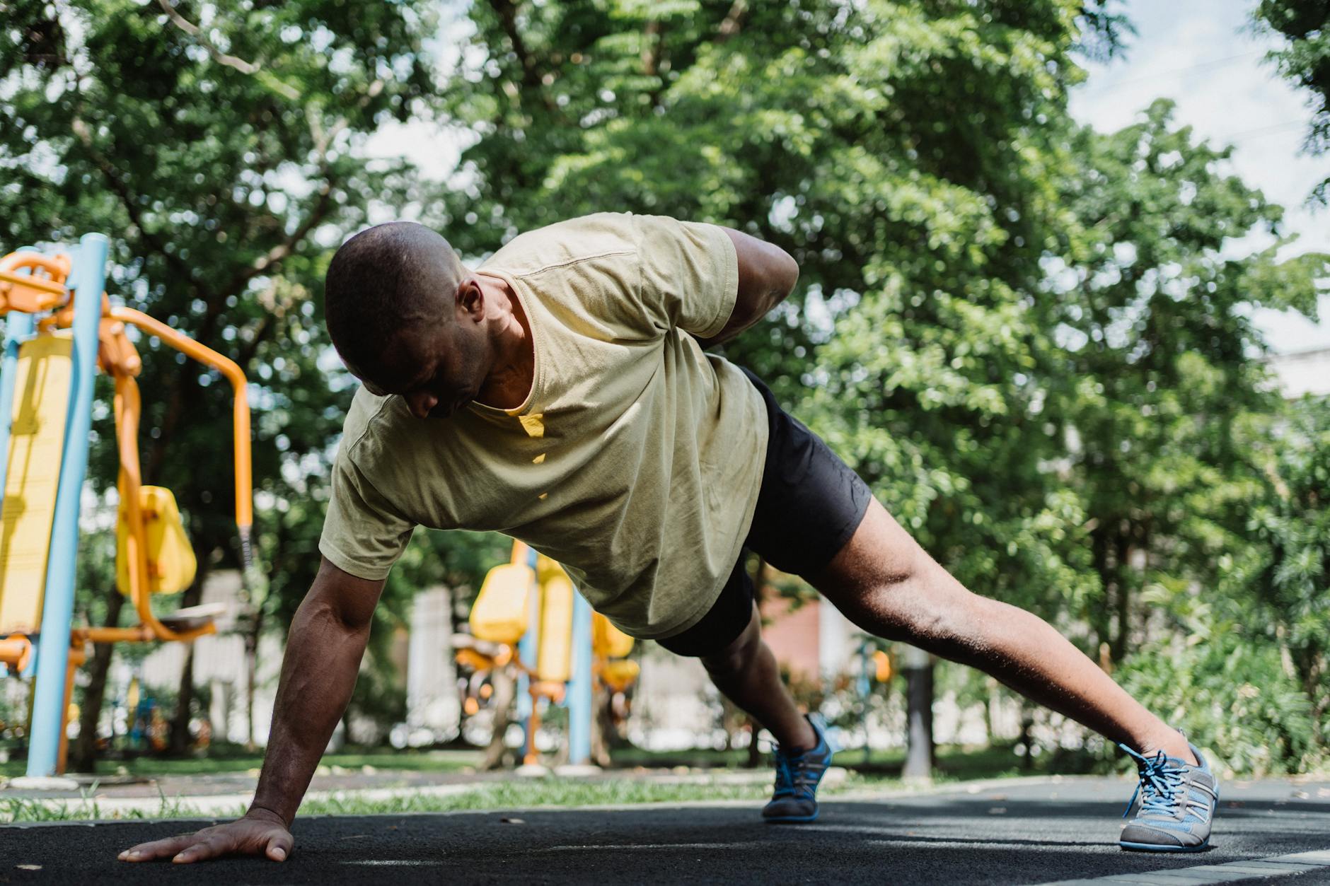 Fit man doing a one-arm push-up outdoors in a park setting, emphasizing strength and endurance. - bodyweight cardio