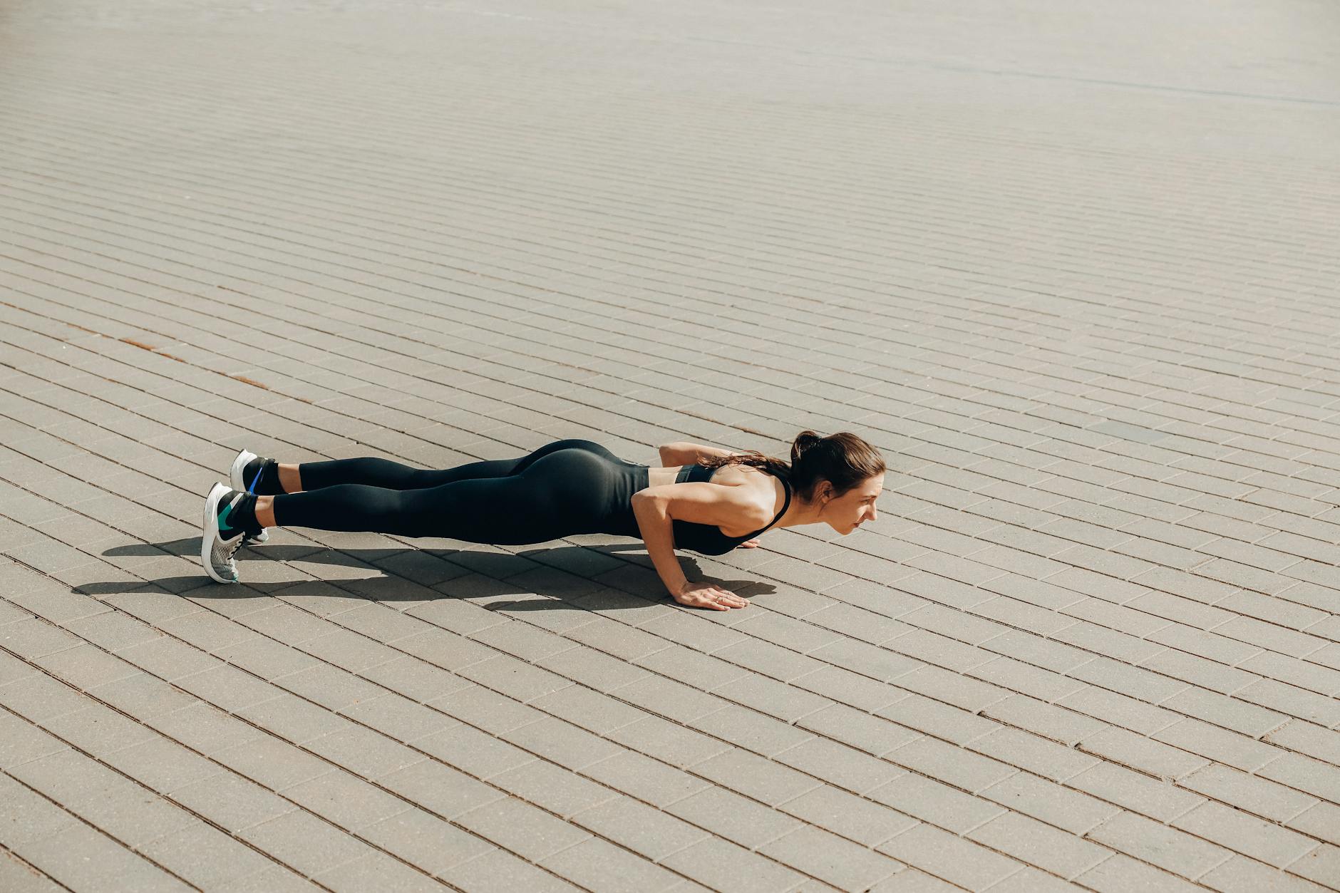 Fit woman in activewear performing push-ups outdoors on a sunny day. - bodyweight shoulder exercises