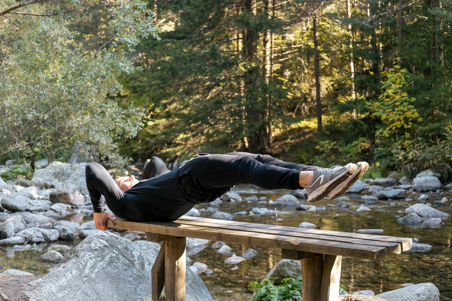 Man performing a core exercise on a bench by a serene river in a forest setting. - bodyweight workouts home