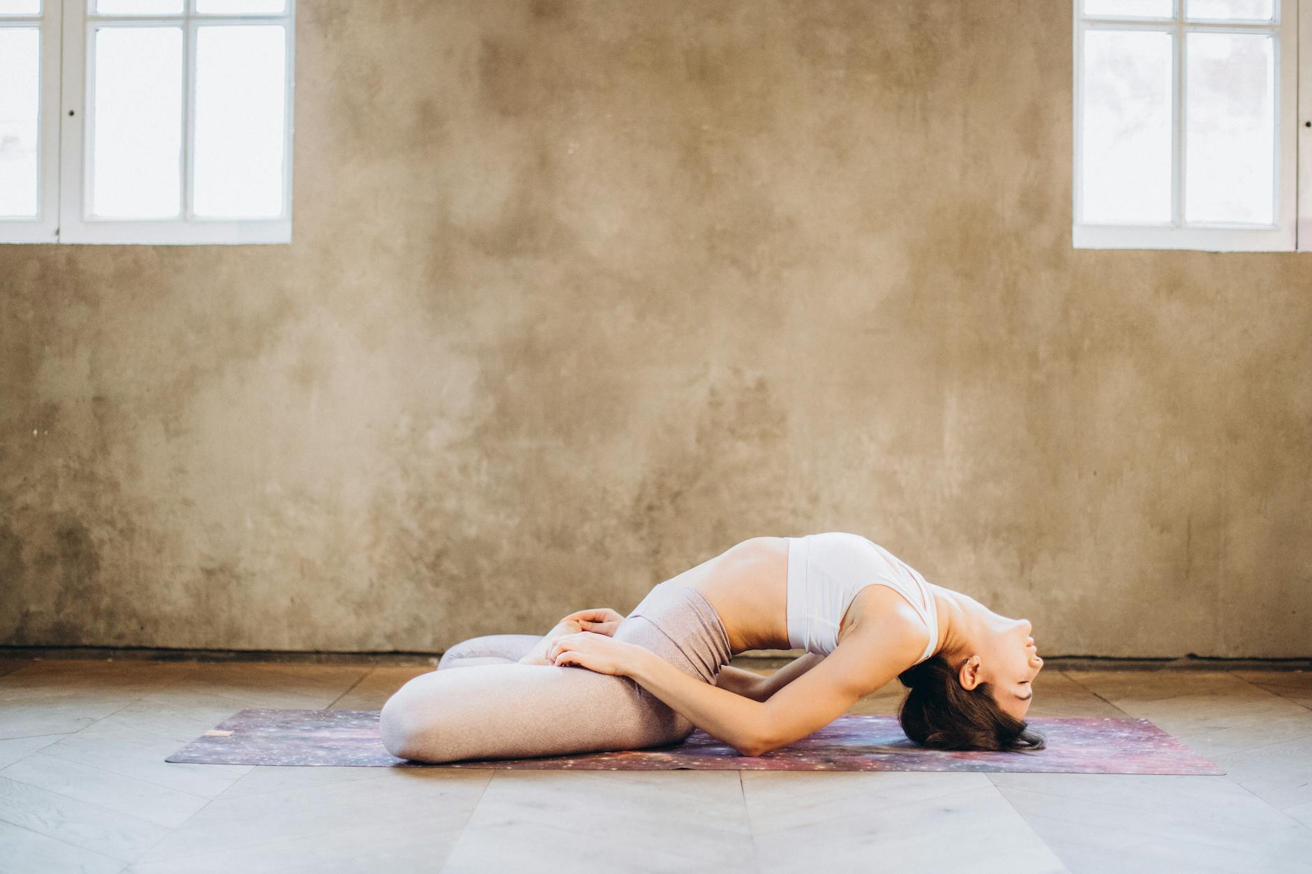 A woman performing Matsyasana yoga pose on a mat indoors, focused on relaxation and wellness. - breathing exercises stress