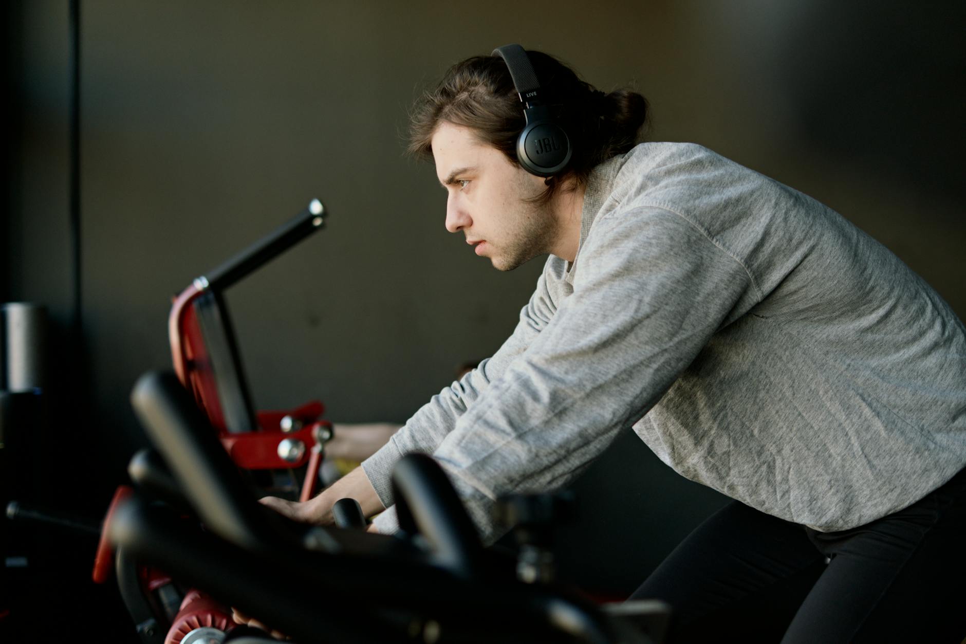 Determined young man training on exercise bike in gym, wearing headphones. - carb cycling workout