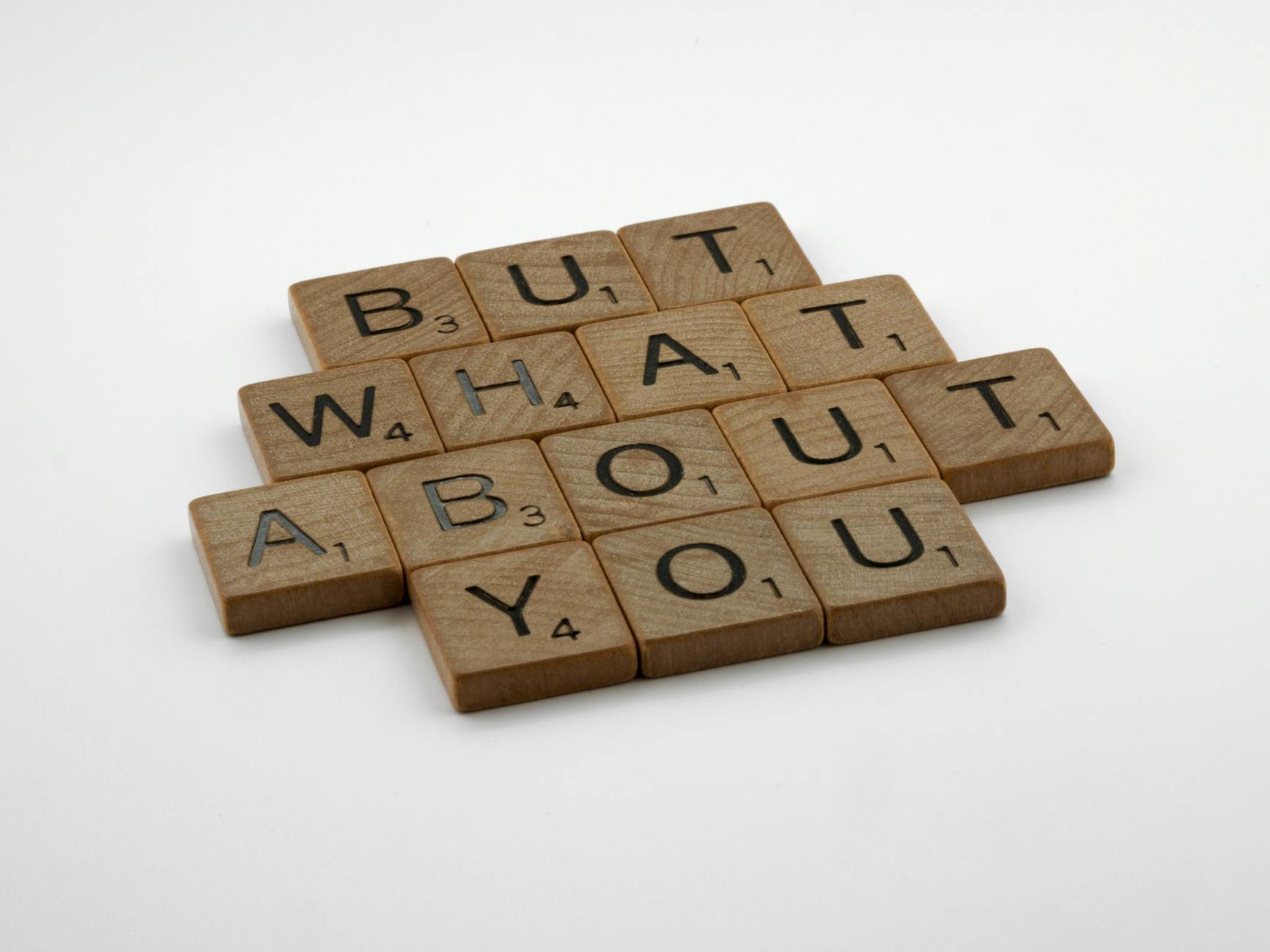 Close-up of wooden Scrabble tiles spelling 'But What About You' on a white surface. - what is core