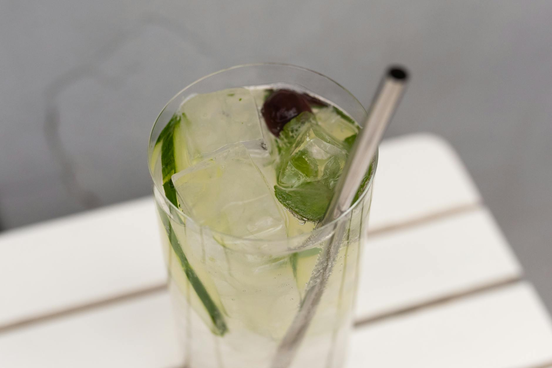 Close-up of a refreshing cucumber cocktail with ice and a metal straw on a wooden table. - cucumber water benefits