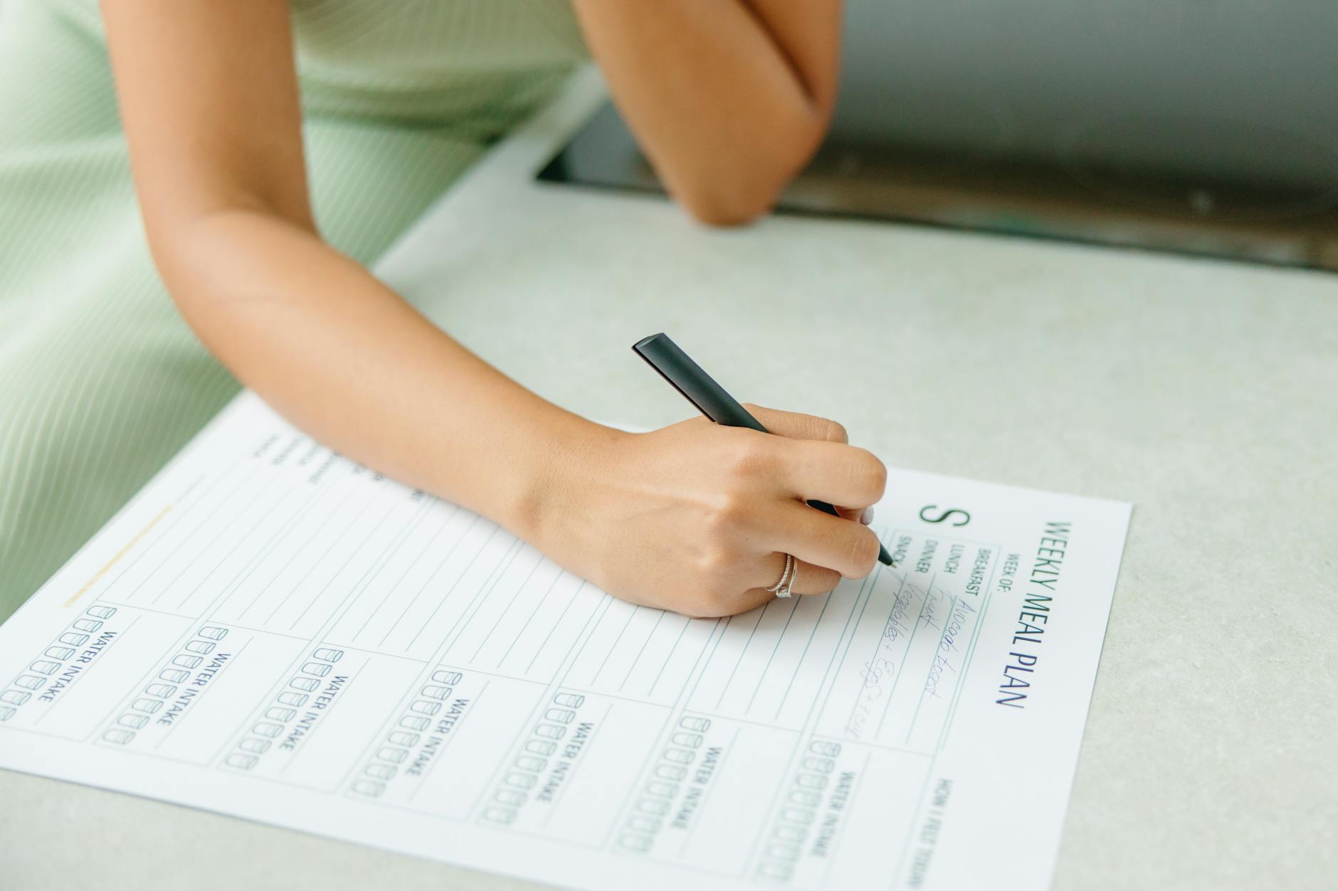Close-up of a woman writing a weekly meal plan at home, promoting a healthy lifestyle. - dash diet plan